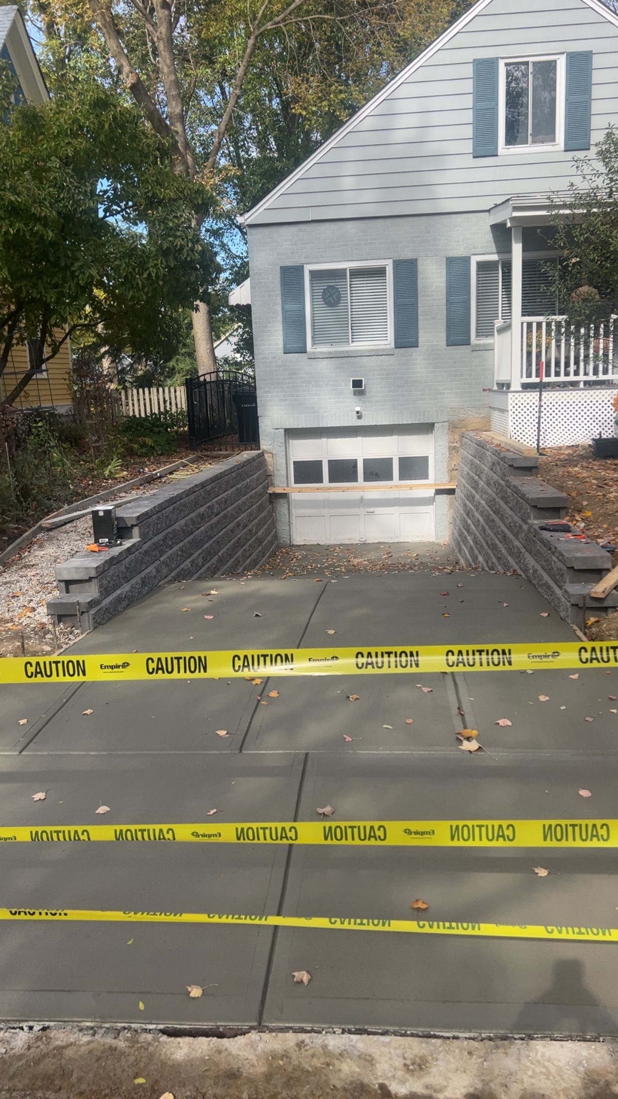 Yellow caution tape blocks a sidewalk beside a white house with a front stoop and garage window.