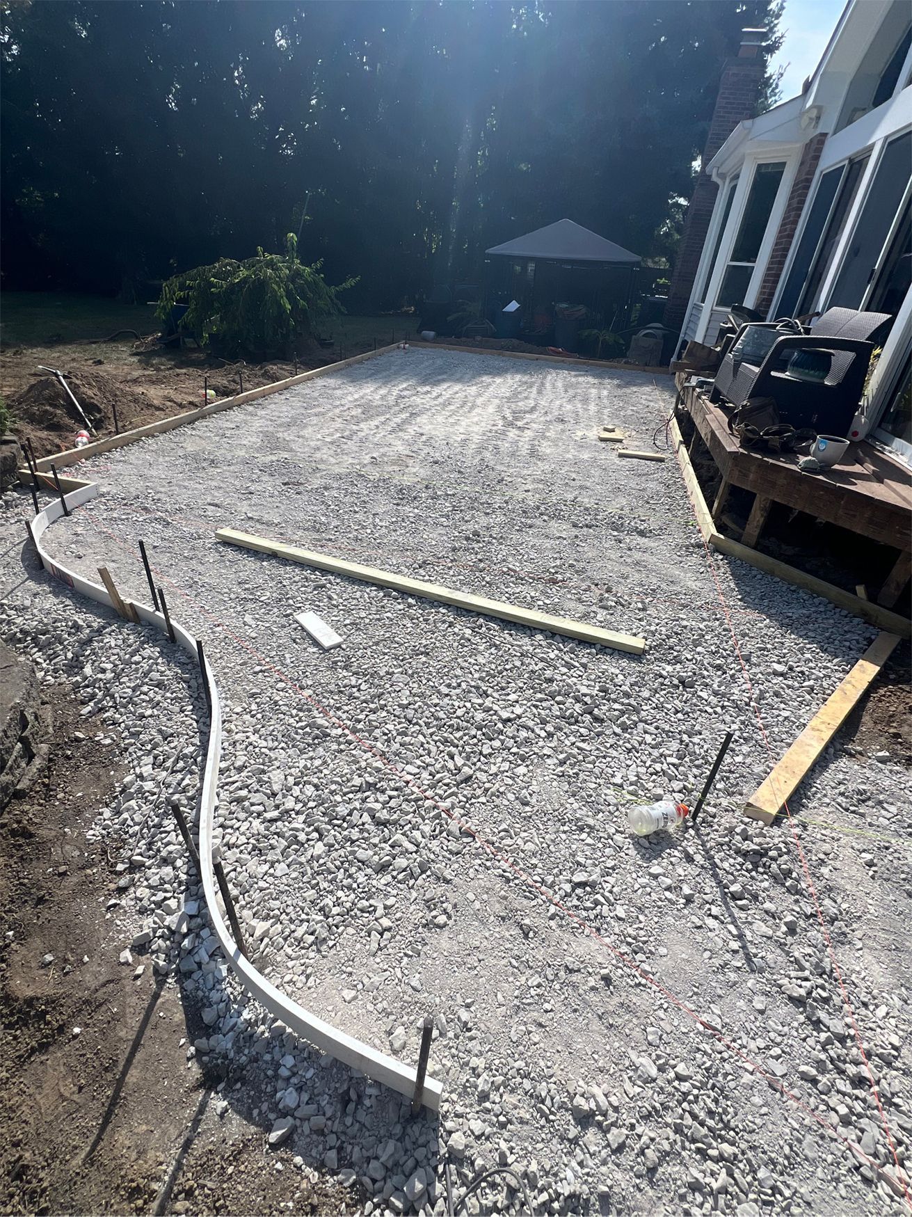 Gravel path under construction beside a house, with edging boards and tools on the ground.