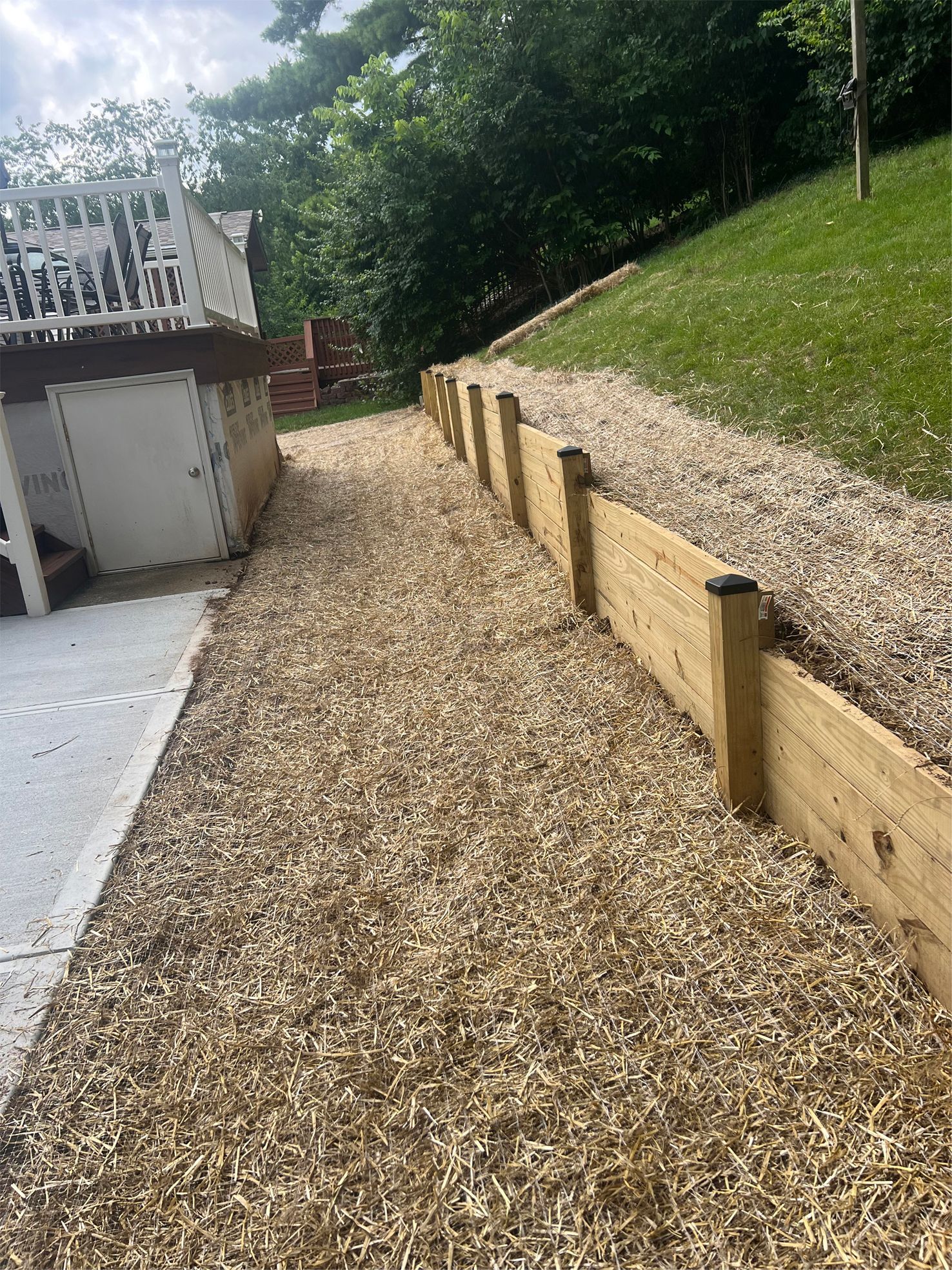 Gravel walkway beside a garage and wooden retaining wall on a sloped, grassy yard