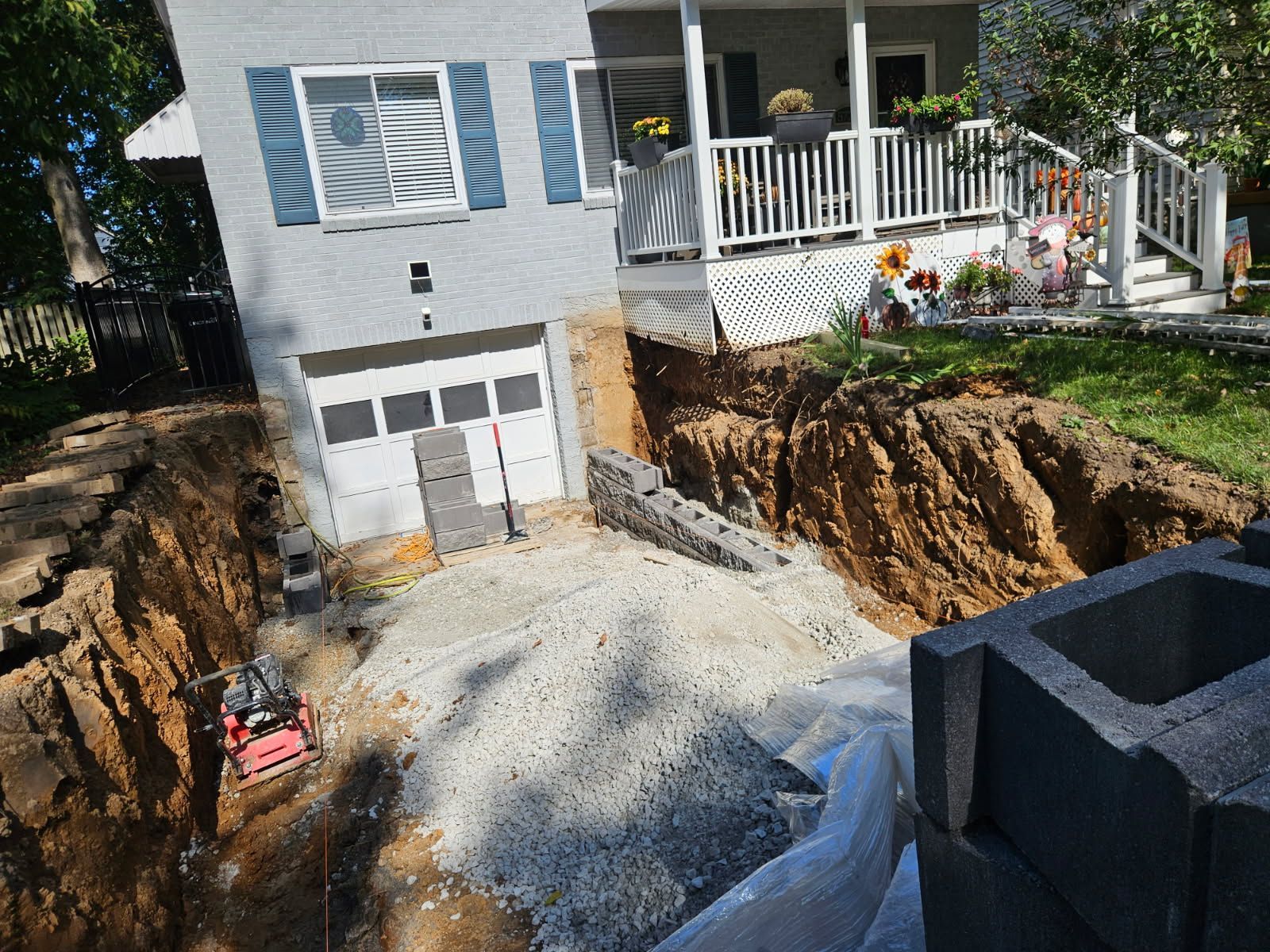 Home driveway under construction beside a house, with gravel, excavated trenches, and a garage below.