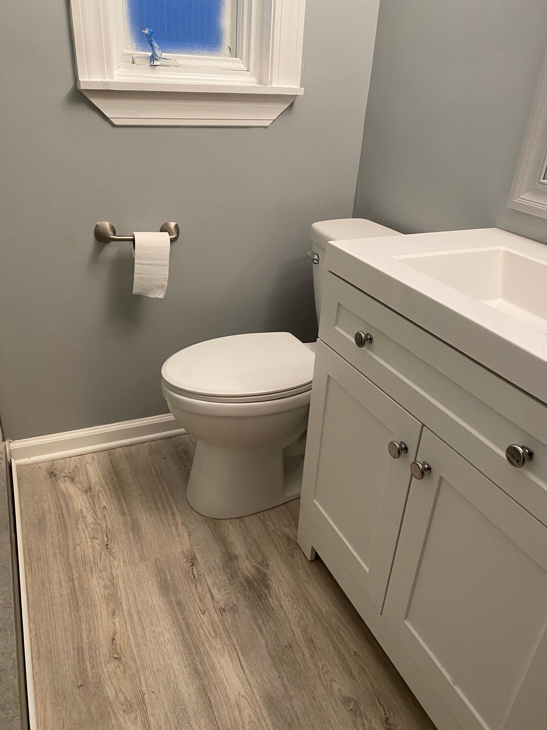 Small bathroom with white toilet, vanity sink, gray walls, and wood-look floor.