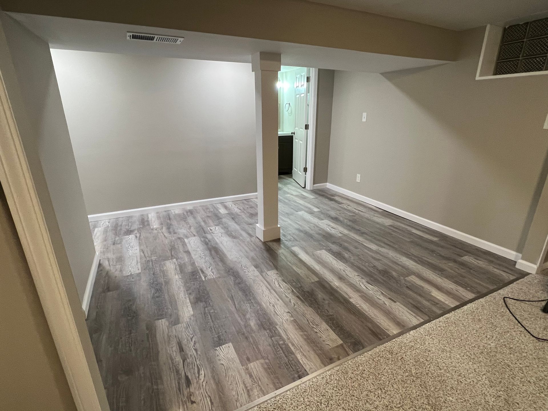 Empty finished basement room with gray wood floors, beige walls, and a support column