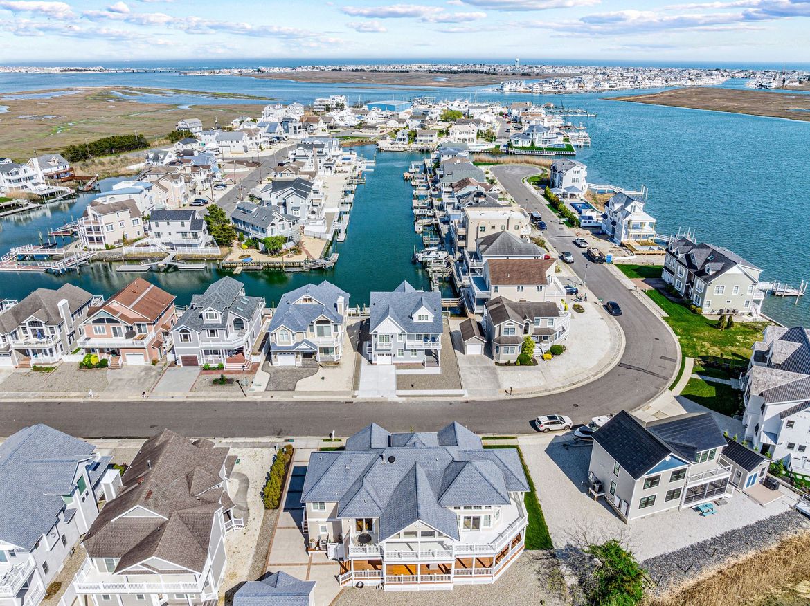 Aerial view of a coastal neighborhood with houses along a waterway and paved streets on a sunny day.