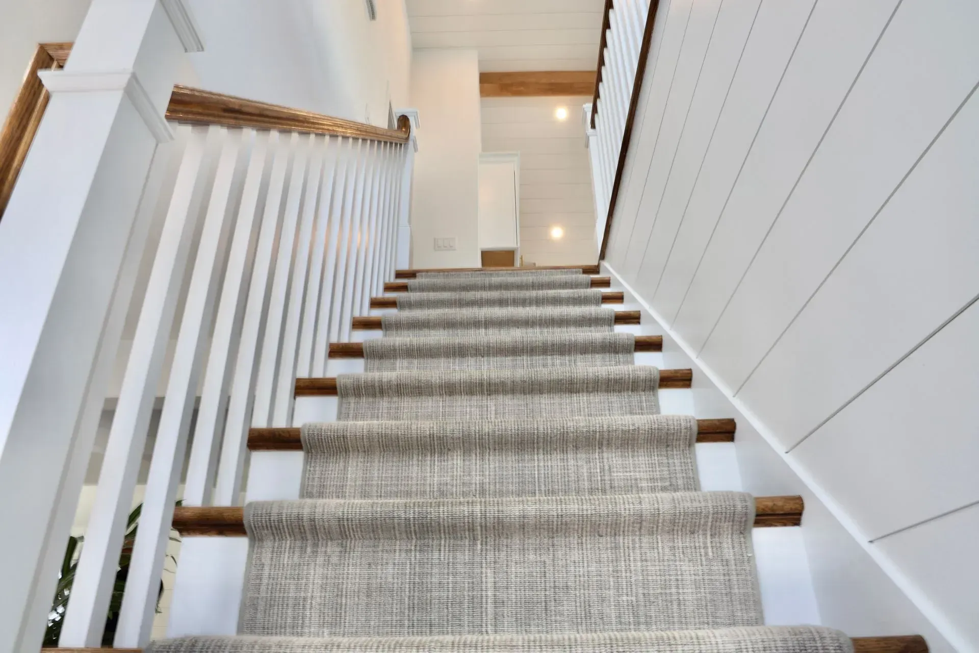 A staircase with white shiplap walls, white railings, a textured grey runner, and wooden stair treads.