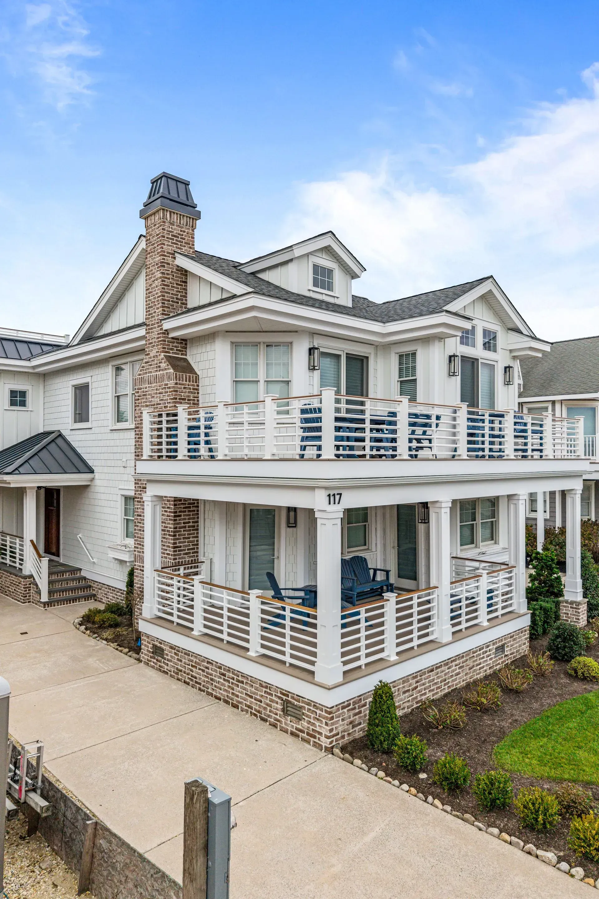 A multi-story house with a white exterior, brick chimney, large wraparound porches, and a paved driveway.