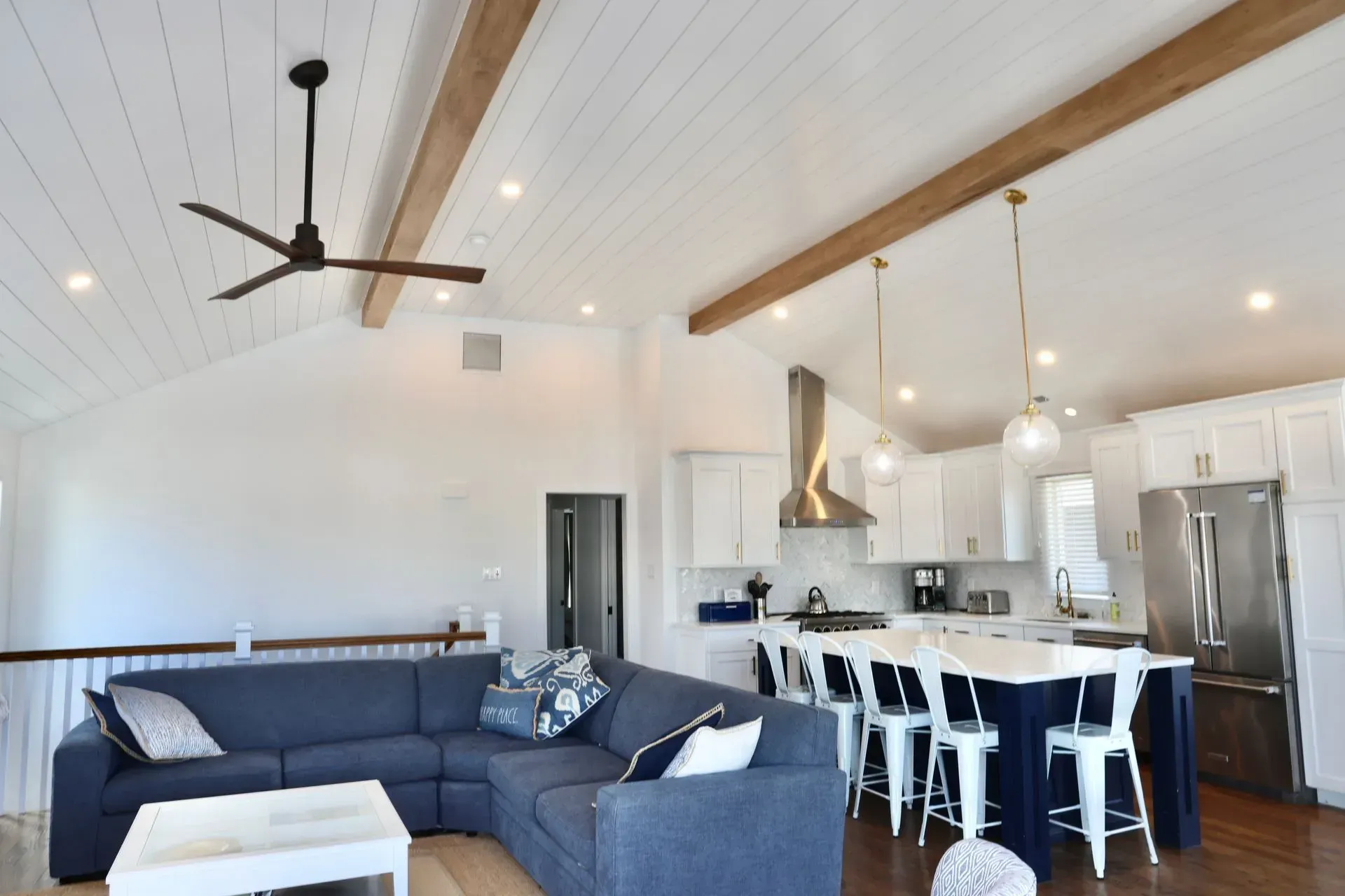 A modern open-concept living area with a blue sectional sofa, kitchen island with stools, and white vaulted ceilings.