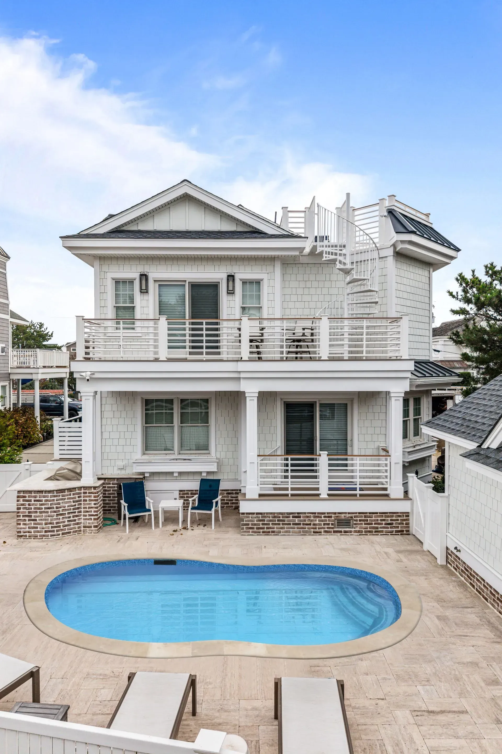 Two-story white house with a patio and swimming pool, featuring a spiral staircase leading to a rooftop deck.