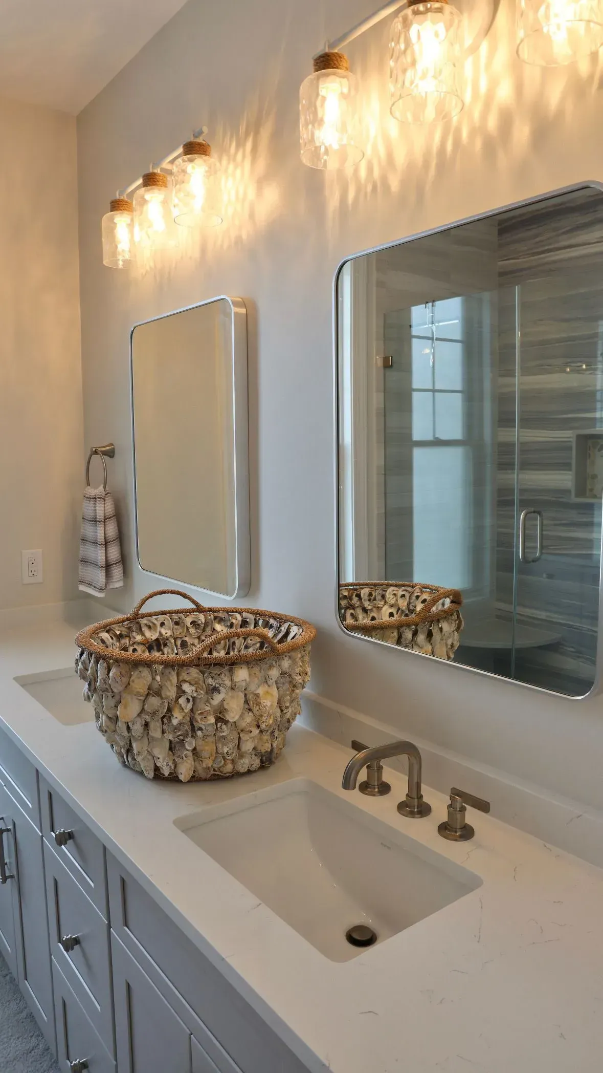 A bathroom vanity with gray cabinets, a white countertop, two sinks, matching mirrors, and mason jar light fixtures.