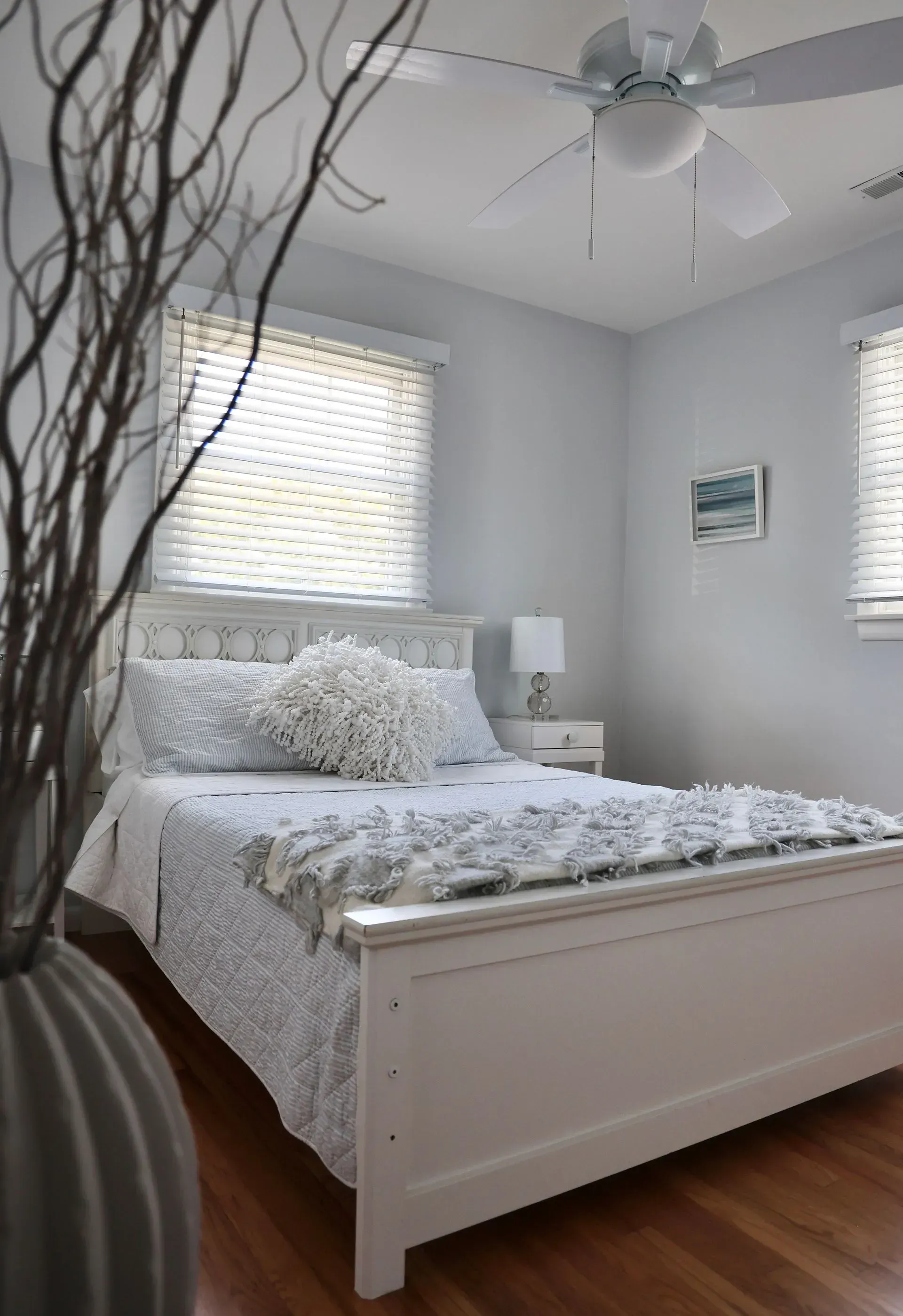 A light blue bedroom with a white bed, patterned bedding, a textured throw, a nightstand, and a ceiling fan.