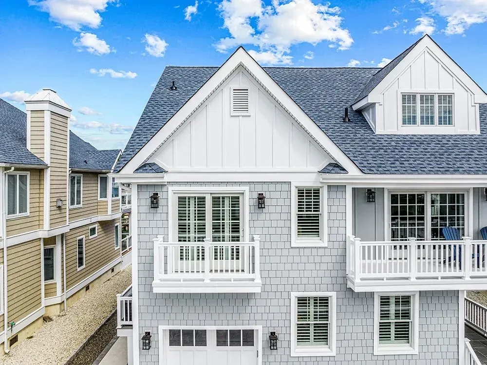 A gray-shingled multi-story residential building with white trim, two balconies, and a blue sky in the background.