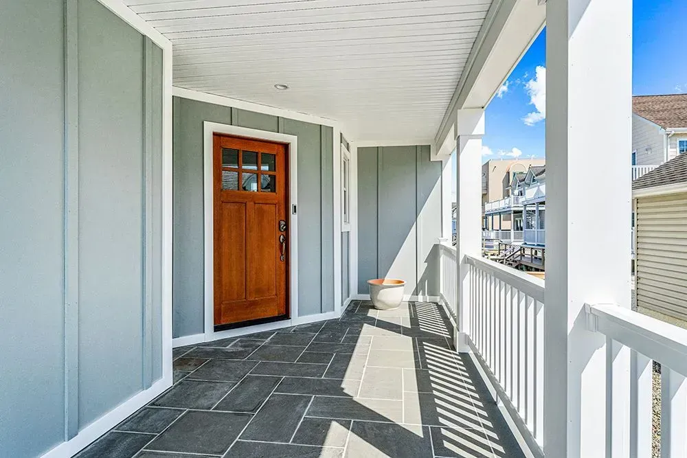 A front porch featuring light gray vertical siding, a natural wood door with glass panes, and dark stone tile flooring.