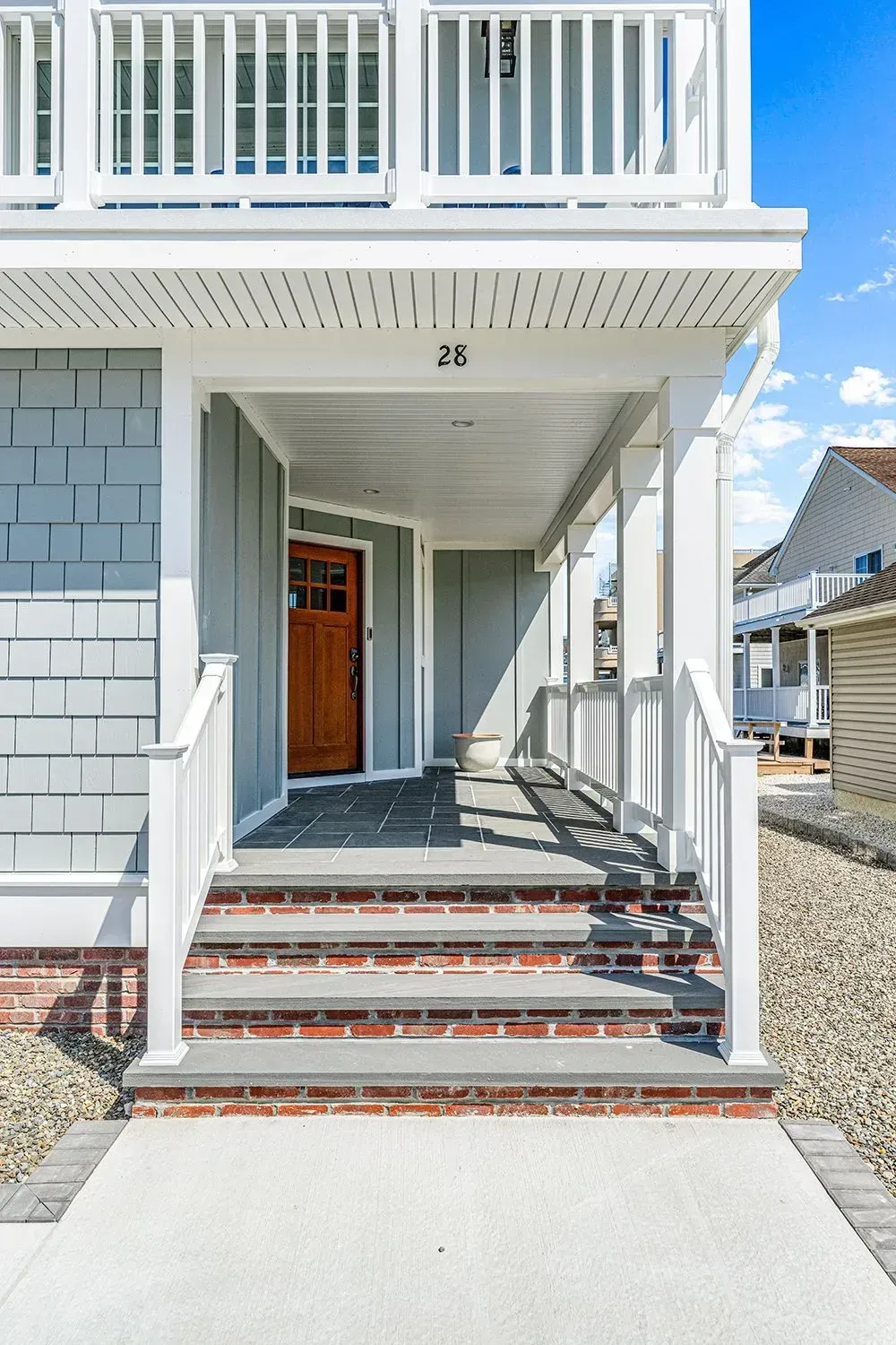 Entrance of a house with a stained wood front door, light blue siding, and concrete steps leading to a covered porch.
