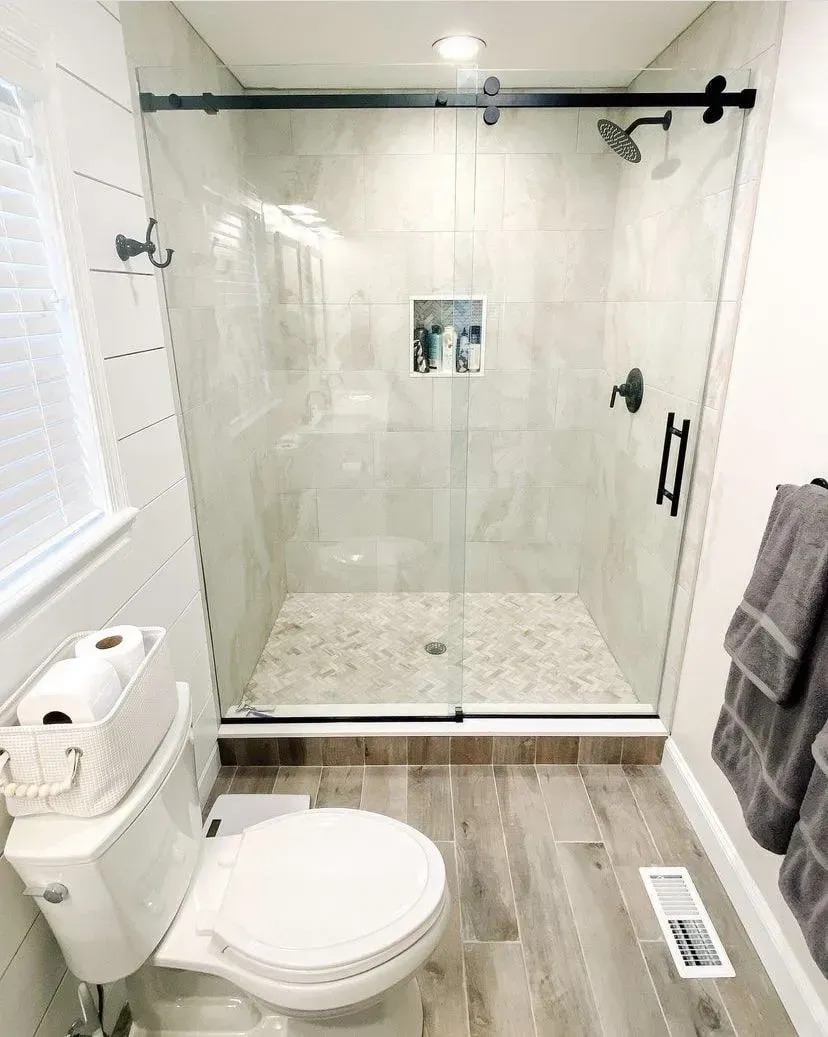 Modern bathroom featuring a glass-enclosed shower, wood-look plank flooring, and a white toilet with a basket of towels.