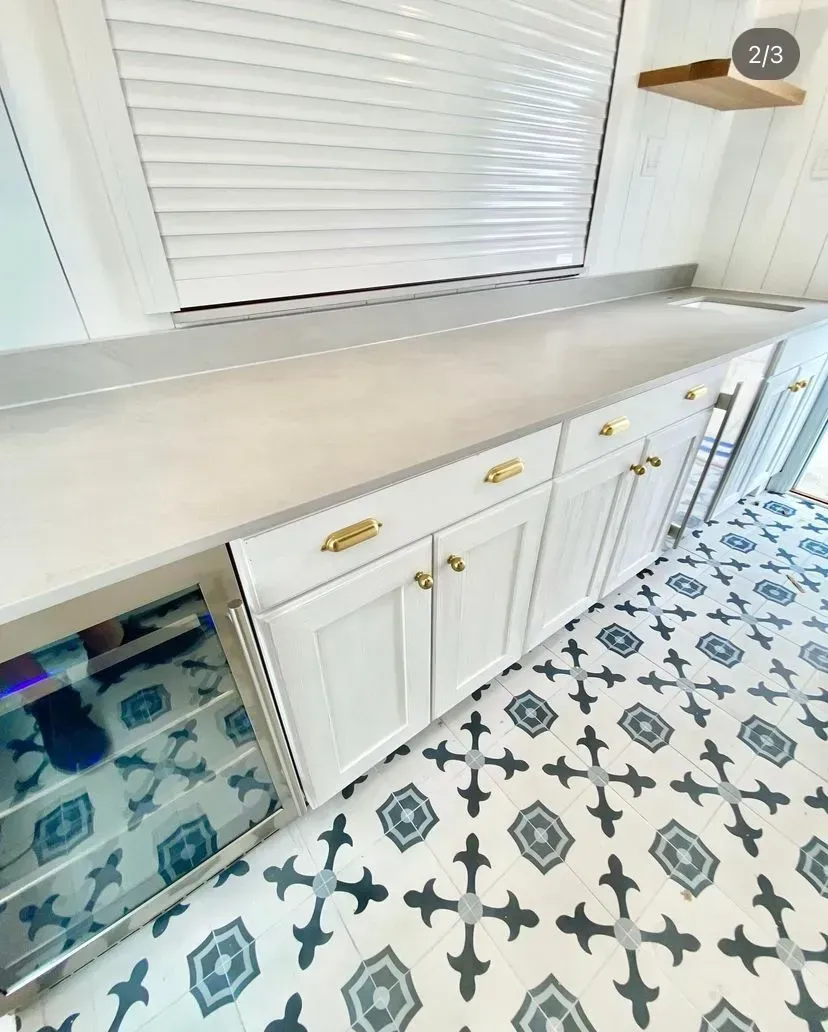 A white kitchen counter with gold hardware, a glass-door beverage fridge, and patterned tile flooring.