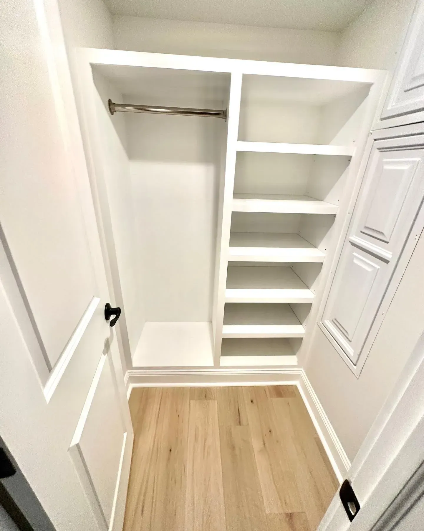 A bright white reach-in closet featuring a hanging rod on the left and six shelves on the right above light wood floors.