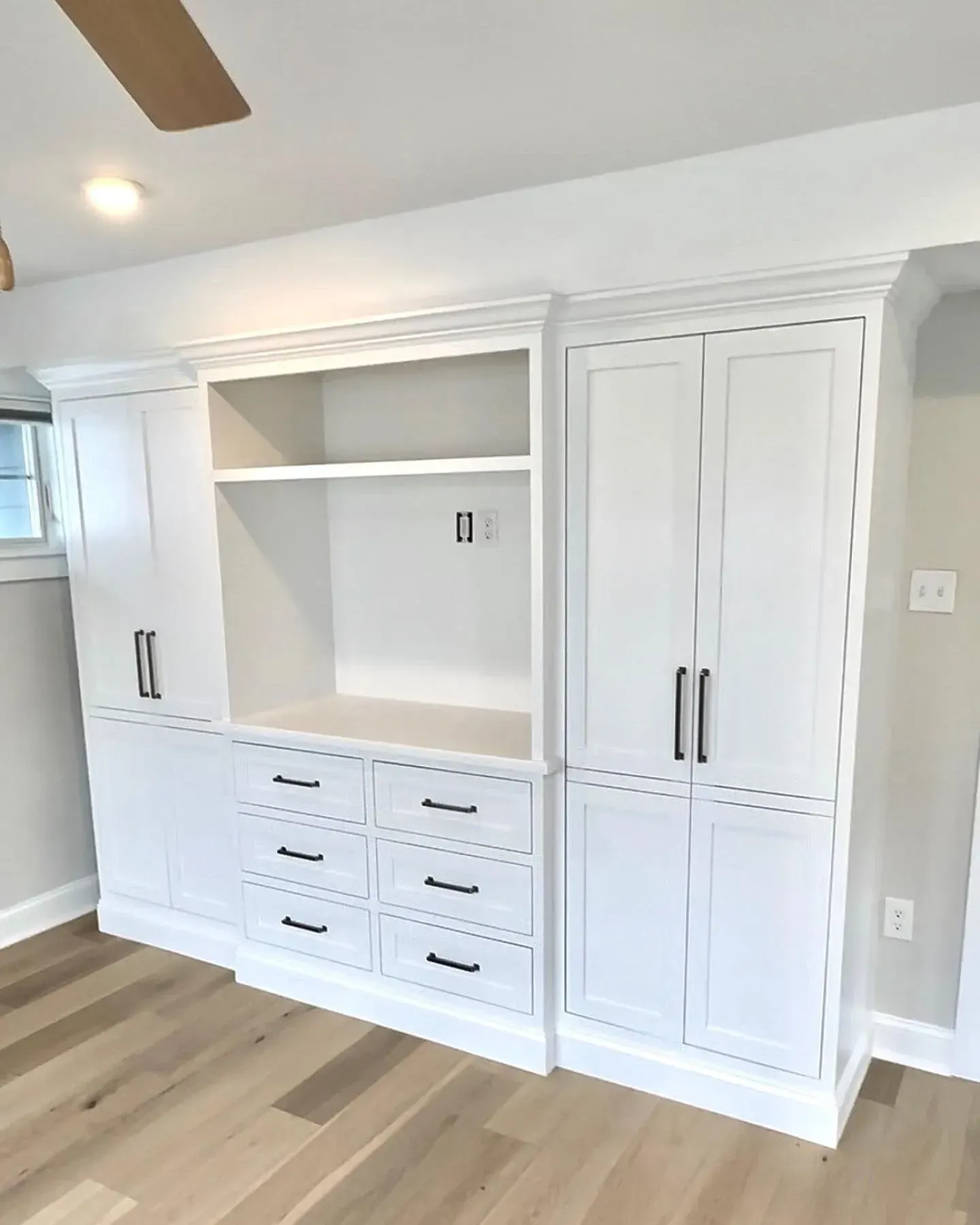 White built-in cabinetry with a center display area, multiple drawers, and two tall side storage closets on wood flooring.