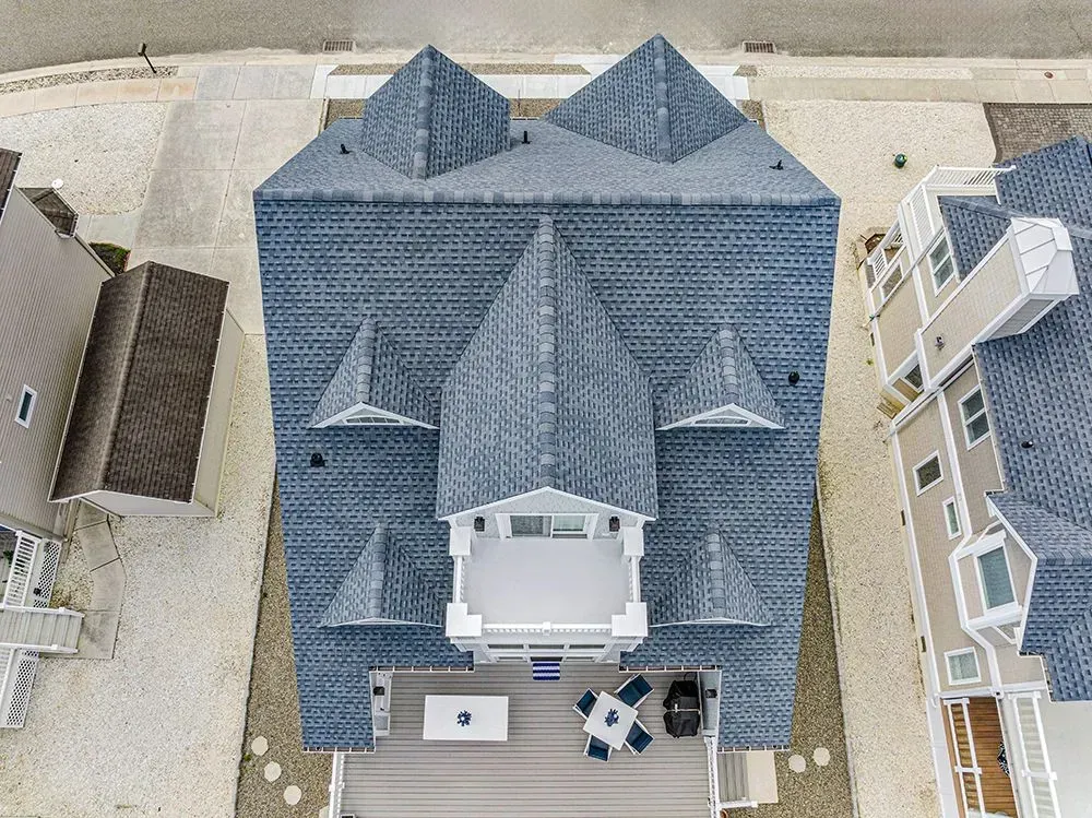 Top-down aerial view of a multi-story house with a complex, shingled roof, a rear deck, and surrounding properties.