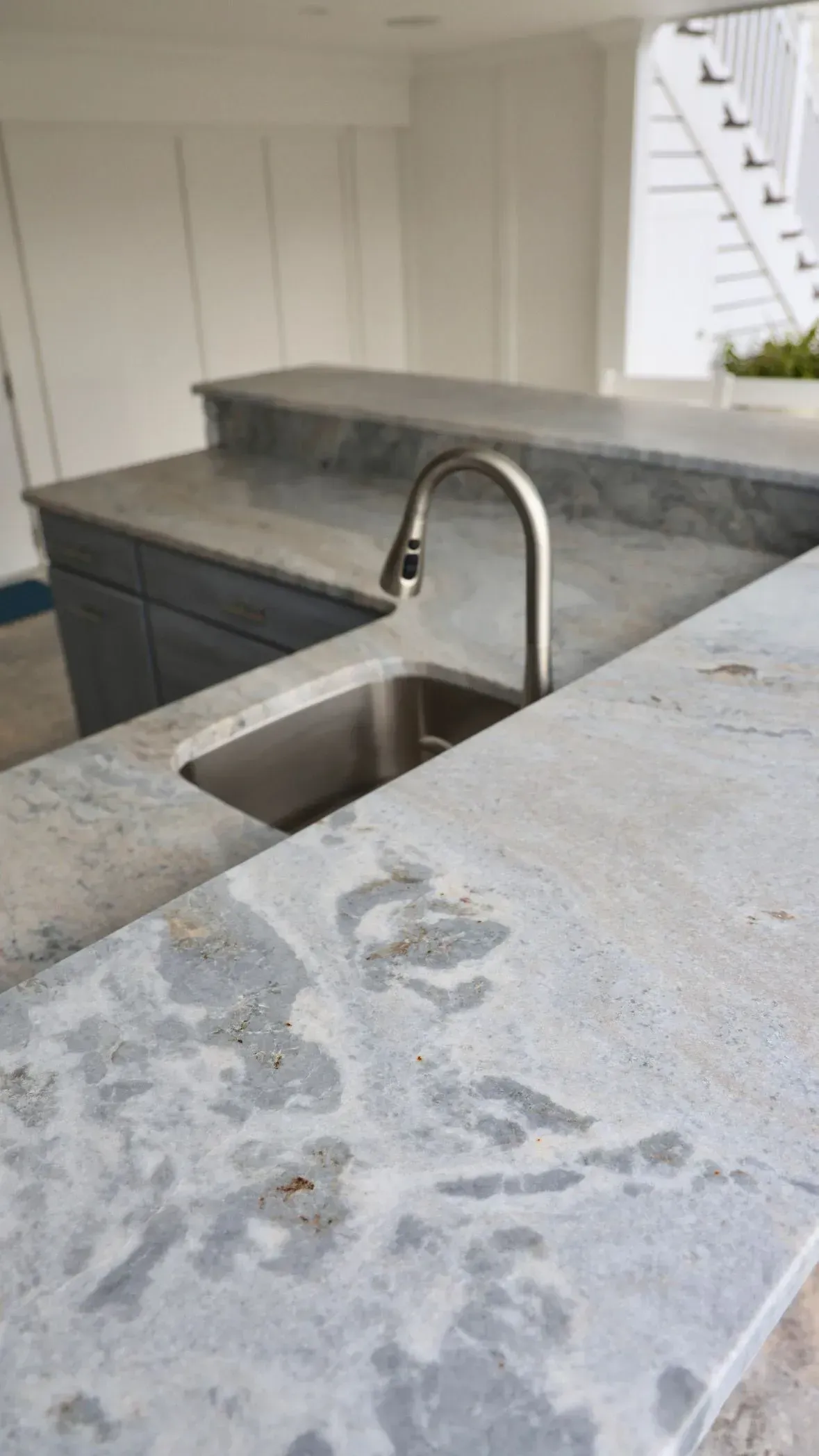 A stainless steel sink and tall faucet set in a light grey granite countertop in a kitchen.
