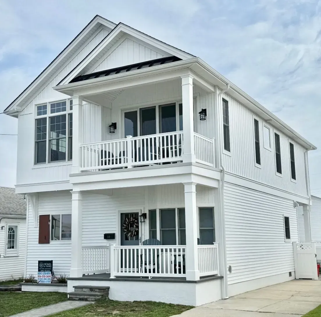 A two-story white house with a double-stacked front porch, board-and-batten siding, and a gabled roof under a cloudy sky.