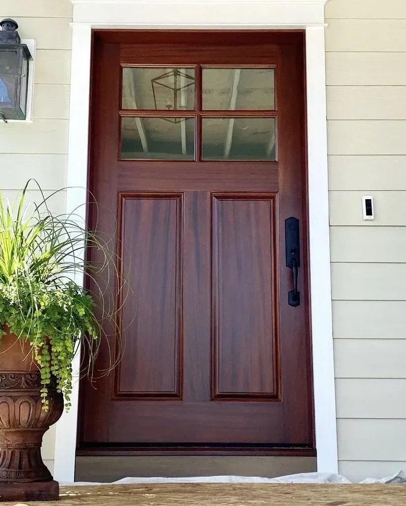 A dark stained wooden front door with a four-pane glass window at the top, installed in a home with cream-colored siding.