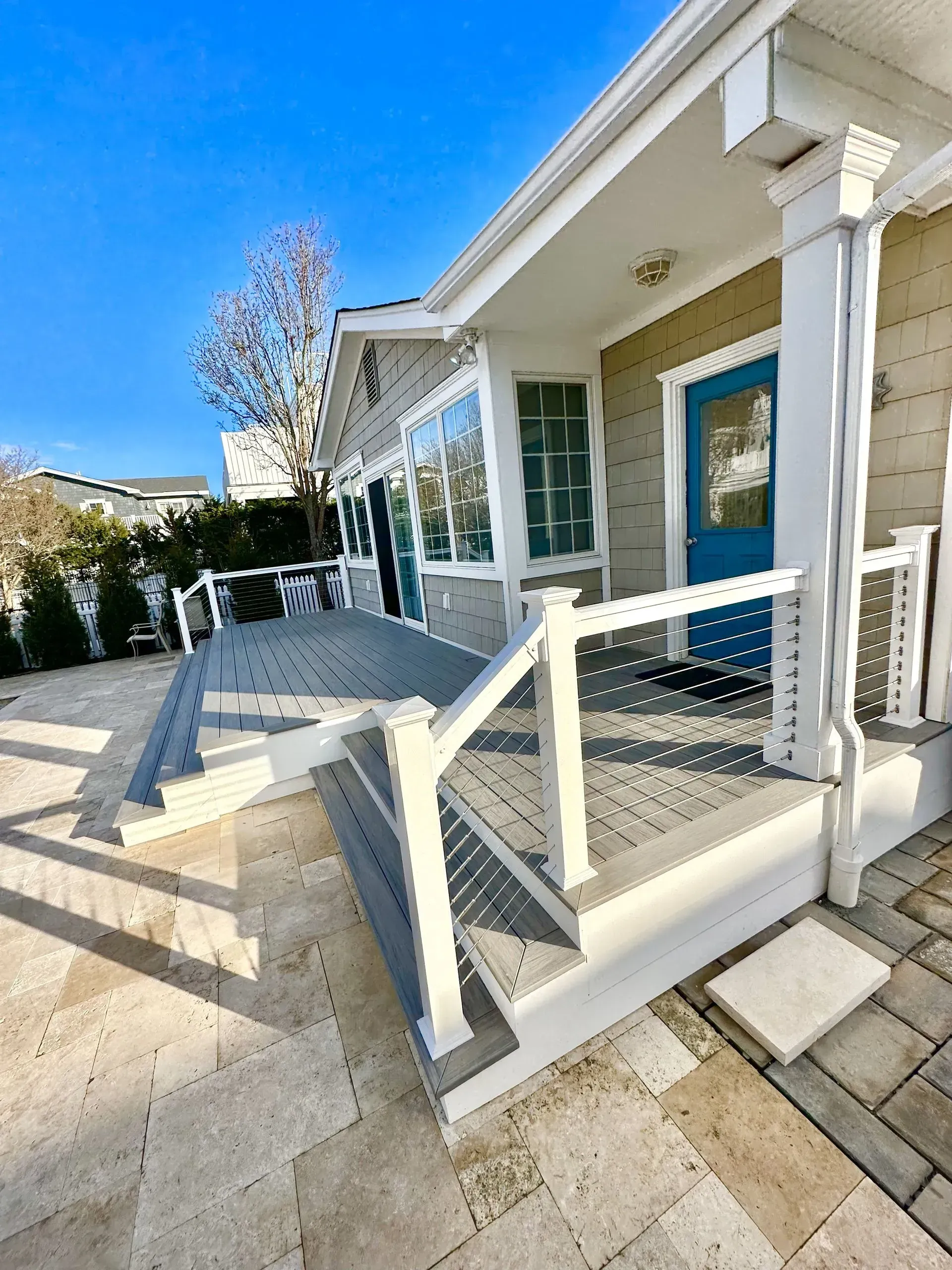 A house exterior featuring a blue front door, white columns, and a gray composite deck with white railings over stone tile.