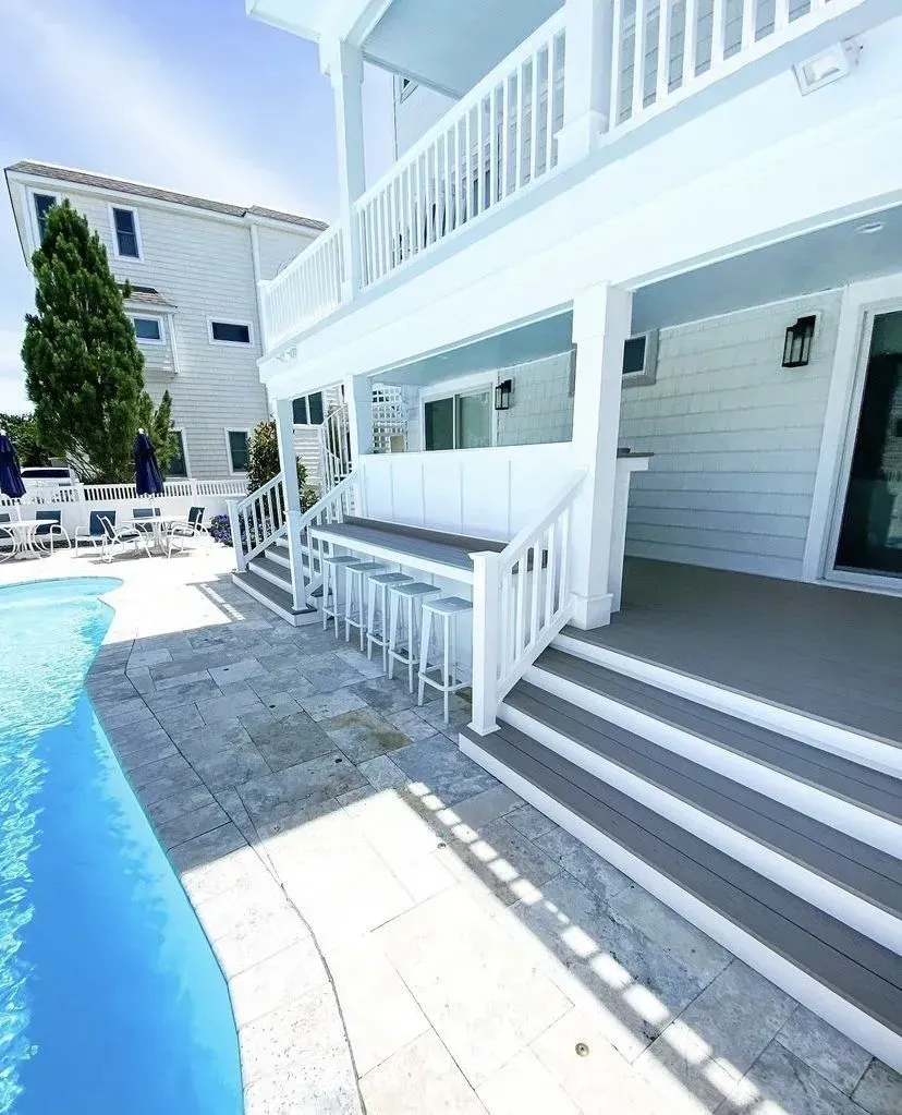 A white multi-story house with a backyard pool, an outdoor bar area, and gray tiered deck steps.