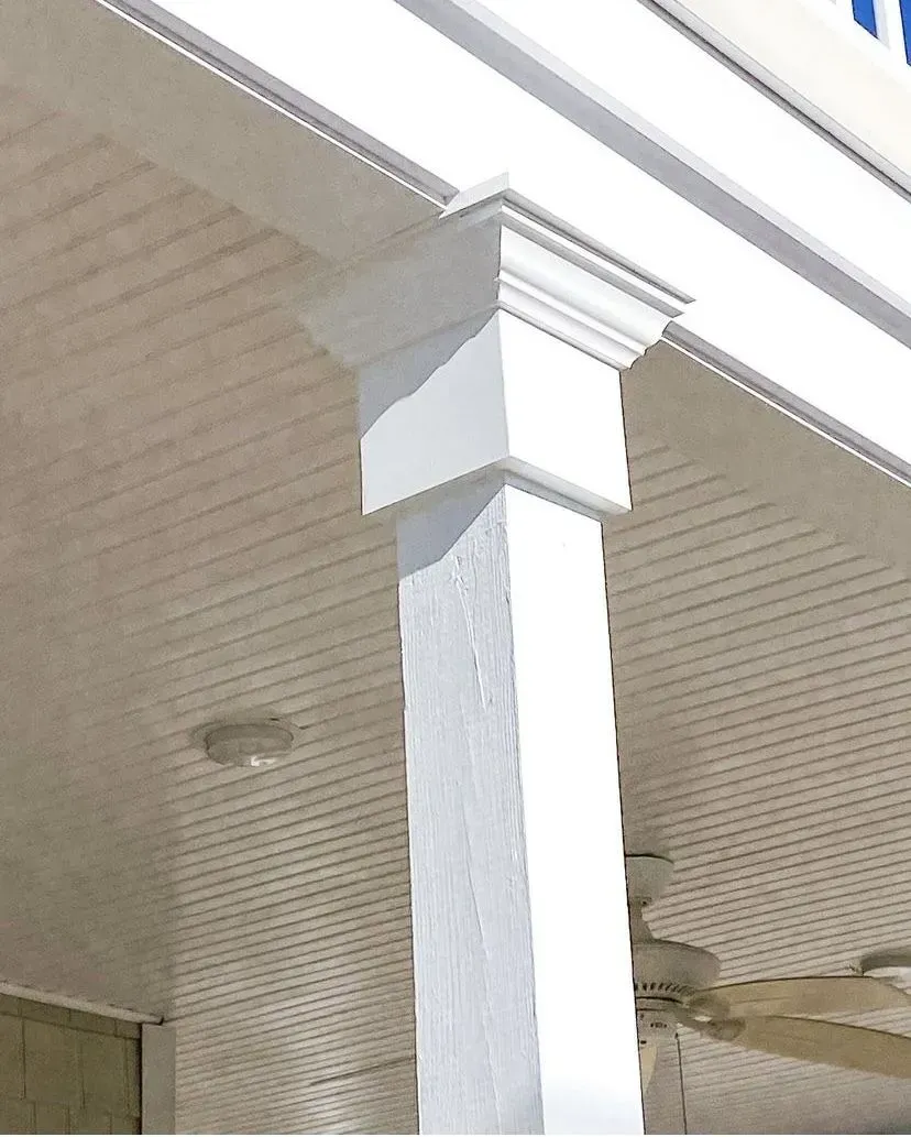 A white, square porch column featuring an ornate capital supporting the roof edge against a beaded porch ceiling.
