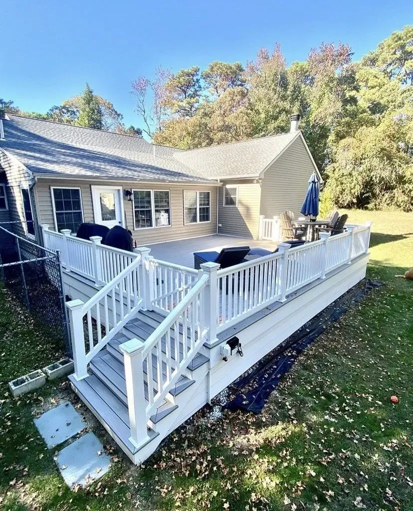 A multi-level backyard deck with white railings and stairs leads to a tan house exterior under a clear blue sky.