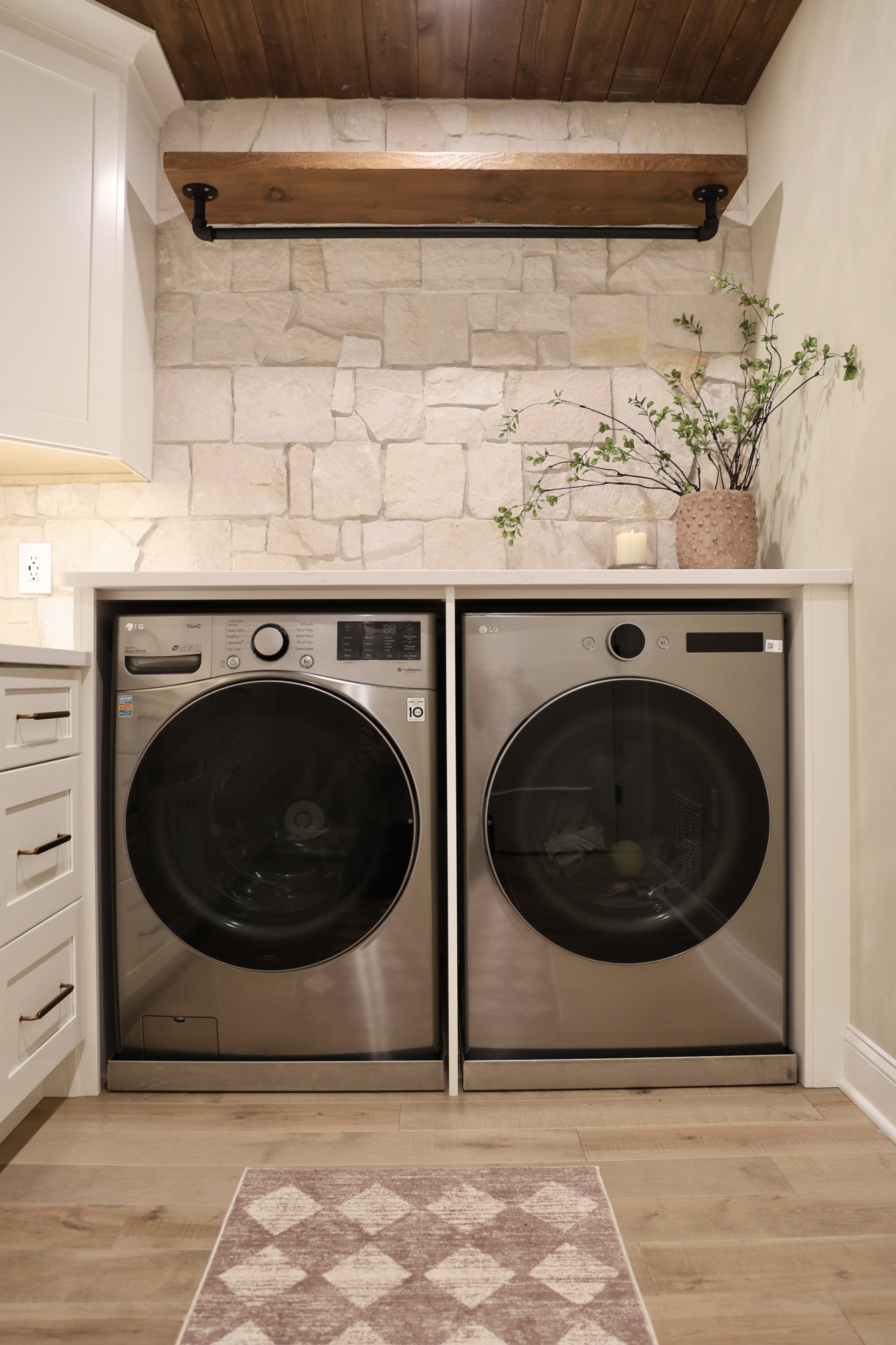 Laundry nook with two front-loading washer-dryer units beneath a counter and wood shelf, with decor above