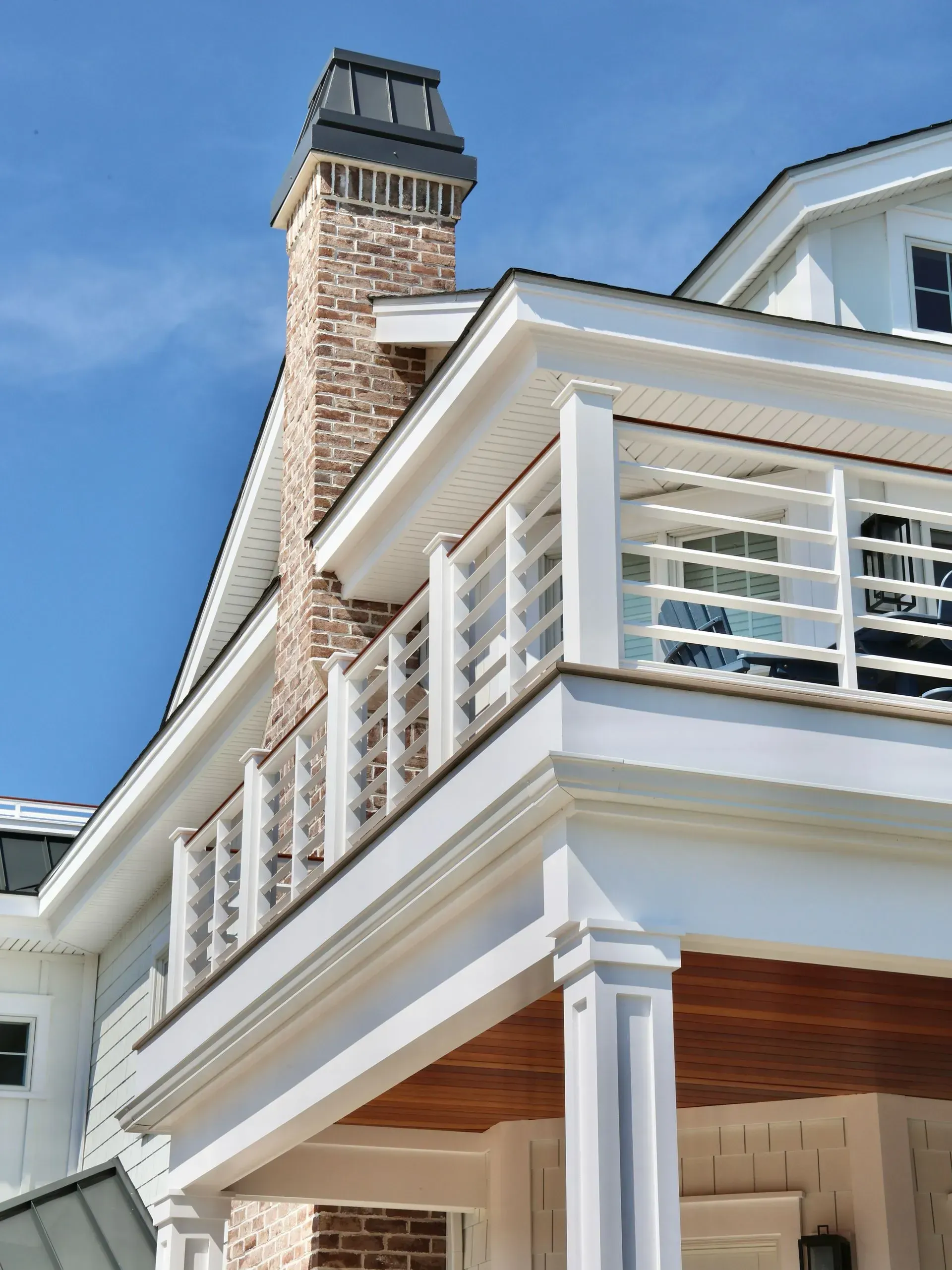 A low-angle view of a white home’s exterior, featuring a stone chimney, wrap-around balcony, and wood-paneled ceiling.