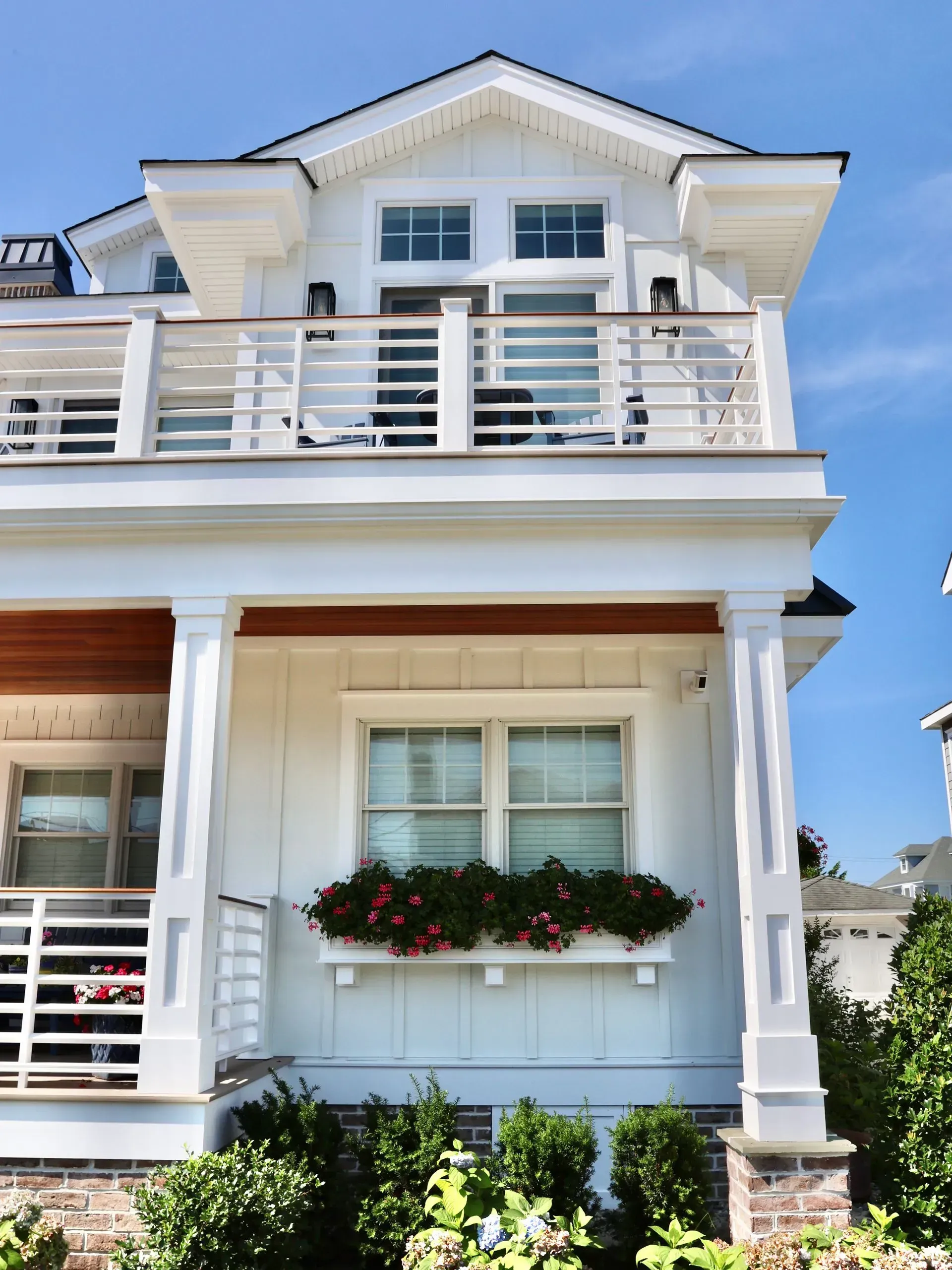 A two-story white house with a balcony, a large window with a flower box, and white porch columns under a blue sky.