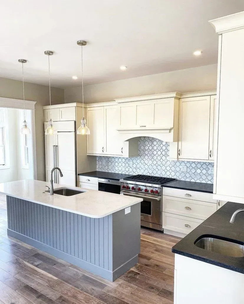 A modern kitchen with a grey island, white cabinets, a black countertop, and a patterned tile backsplash.