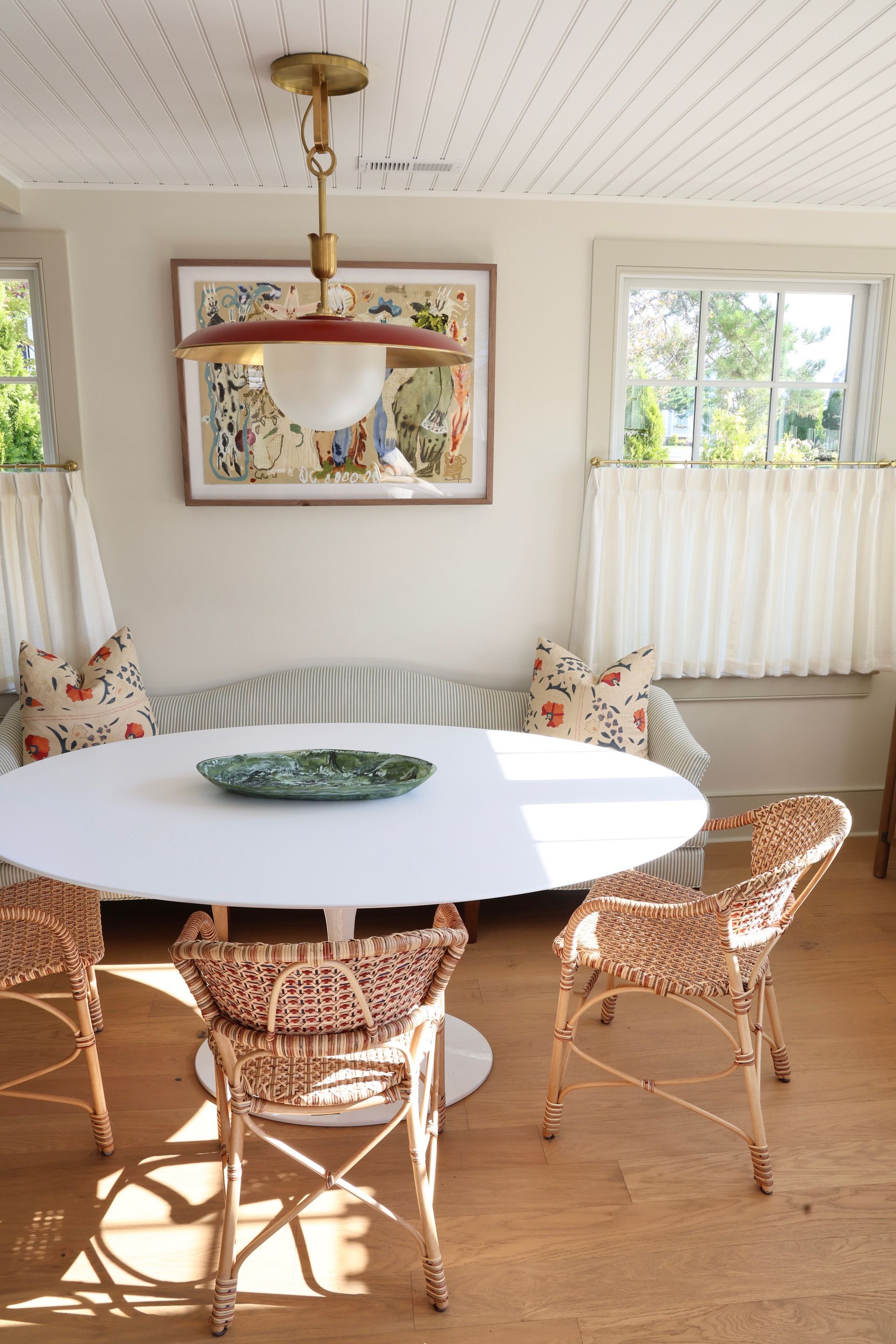 Bright dining nook with white round table, wicker chairs, floral cushions, and large windows.