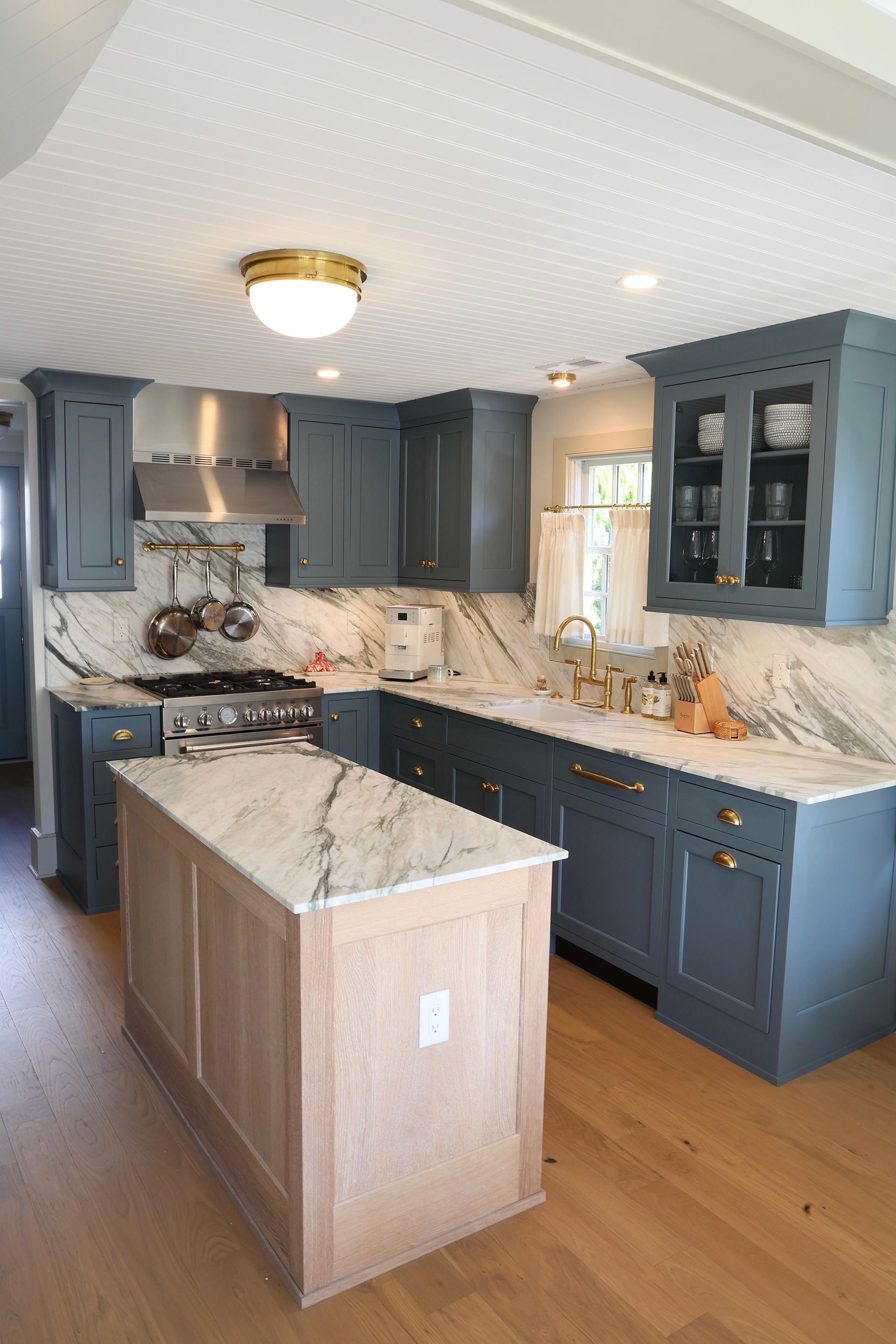 Blue-gray kitchen with marble countertops, island, wood floor, and glass-front cabinets.