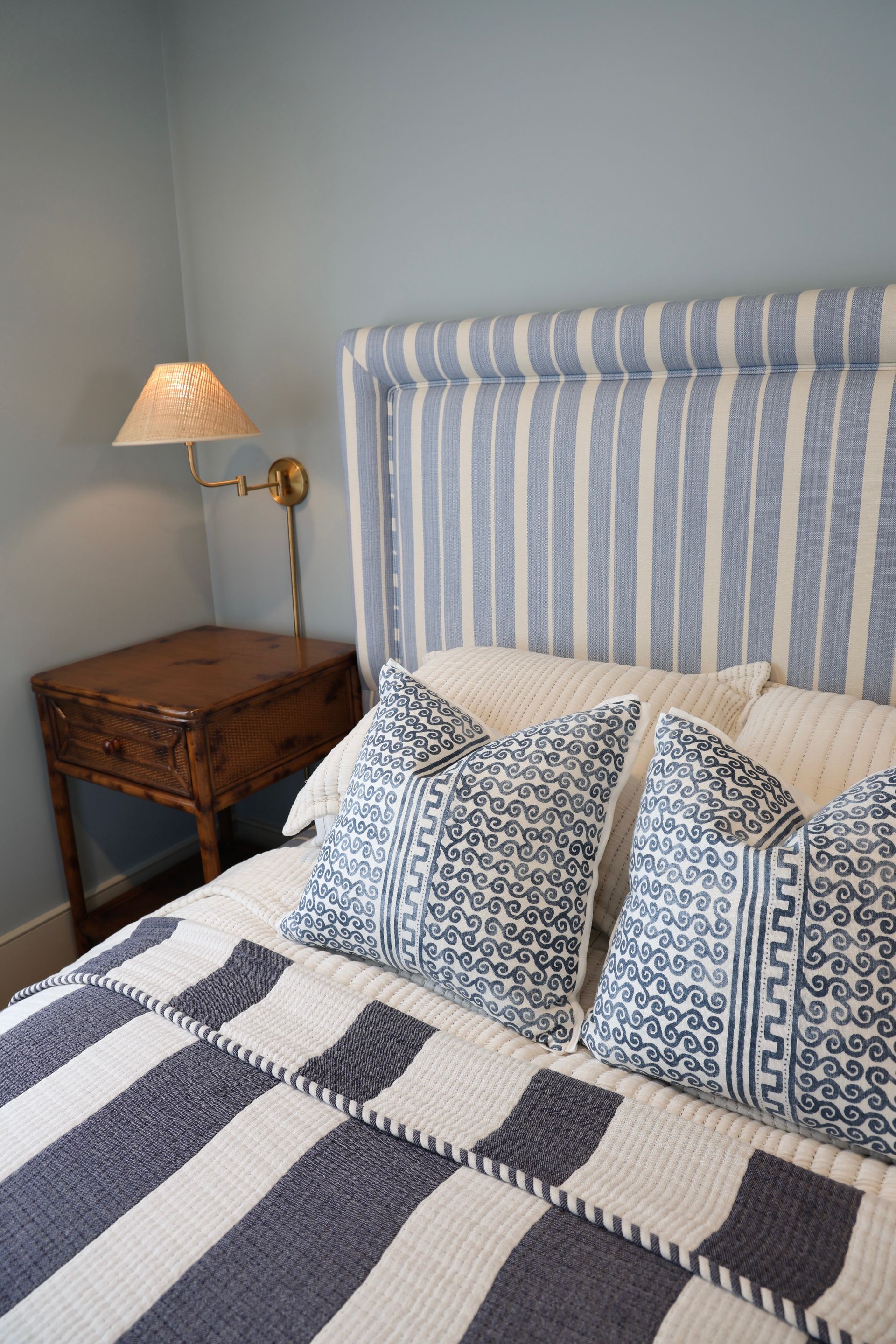 Cozy bedroom with blue striped headboard, patterned pillows, checkered blanket, and bedside lamp.