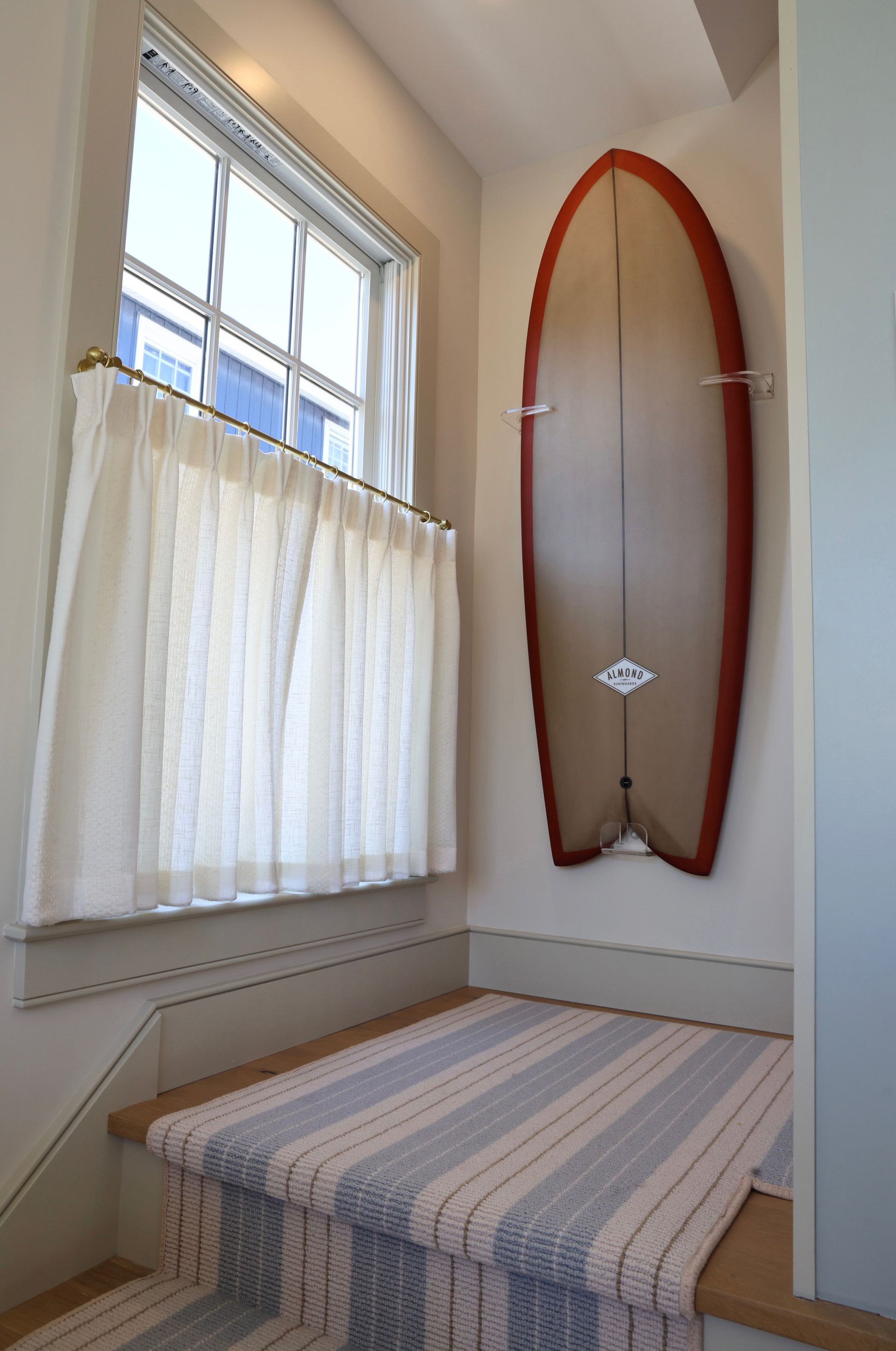Small bedroom nook with a bed, window, and a surfboard mounted on the wall.