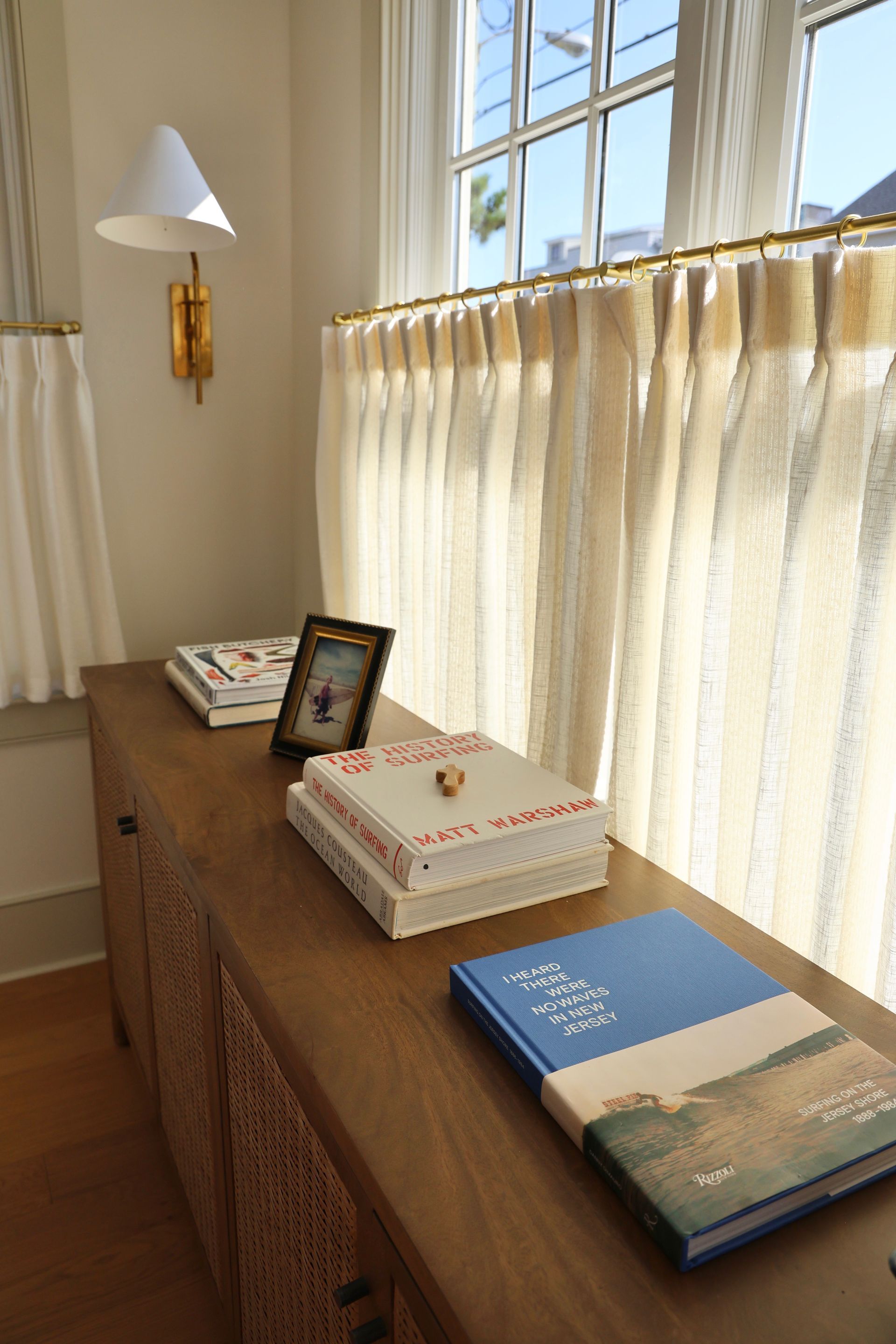 Sunlit windowsill with books, a framed photo, and a gold wall sconce in a cream room.