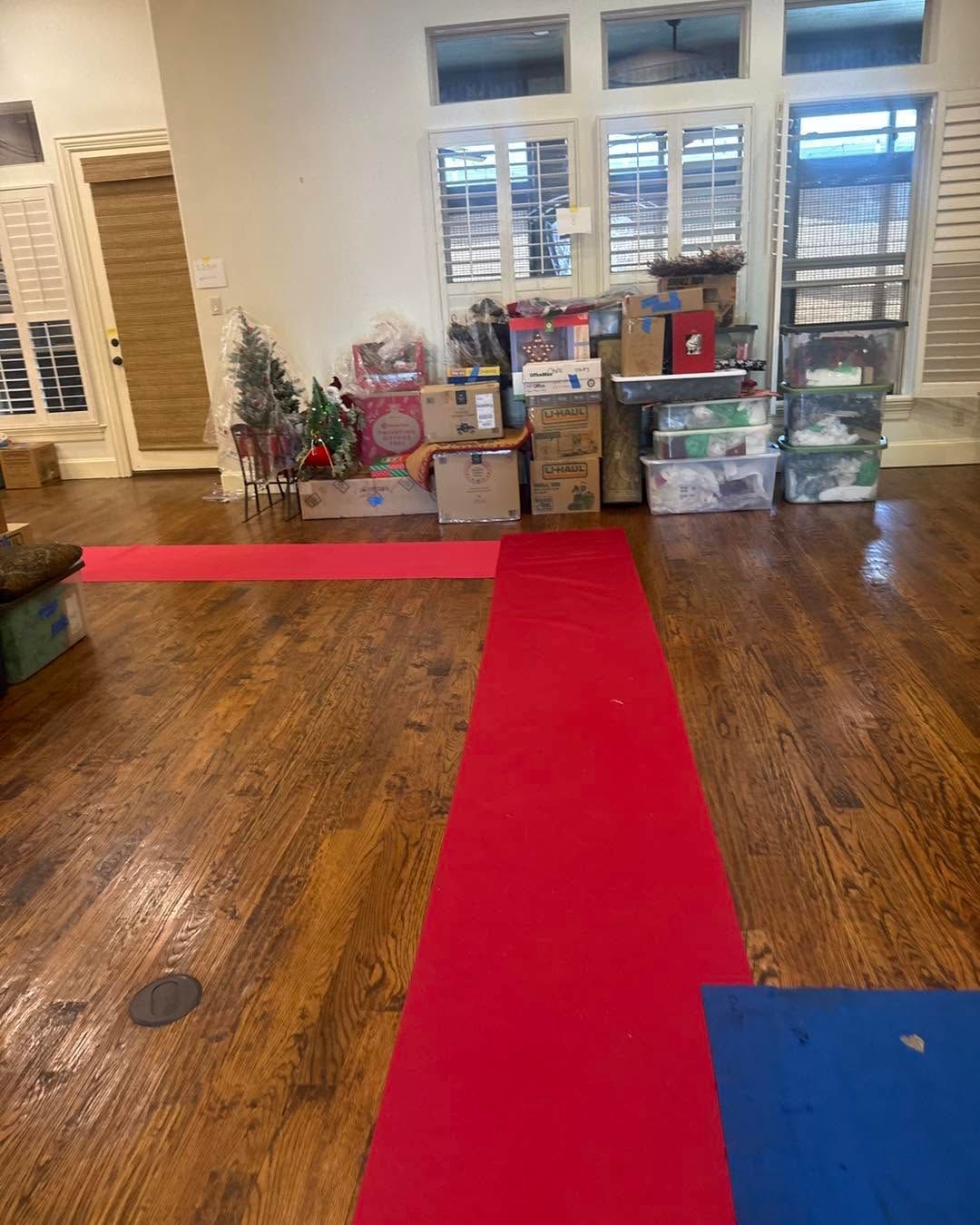 Living room with a red runner on wood floor and stacked boxes by the window, including a small decorated tree