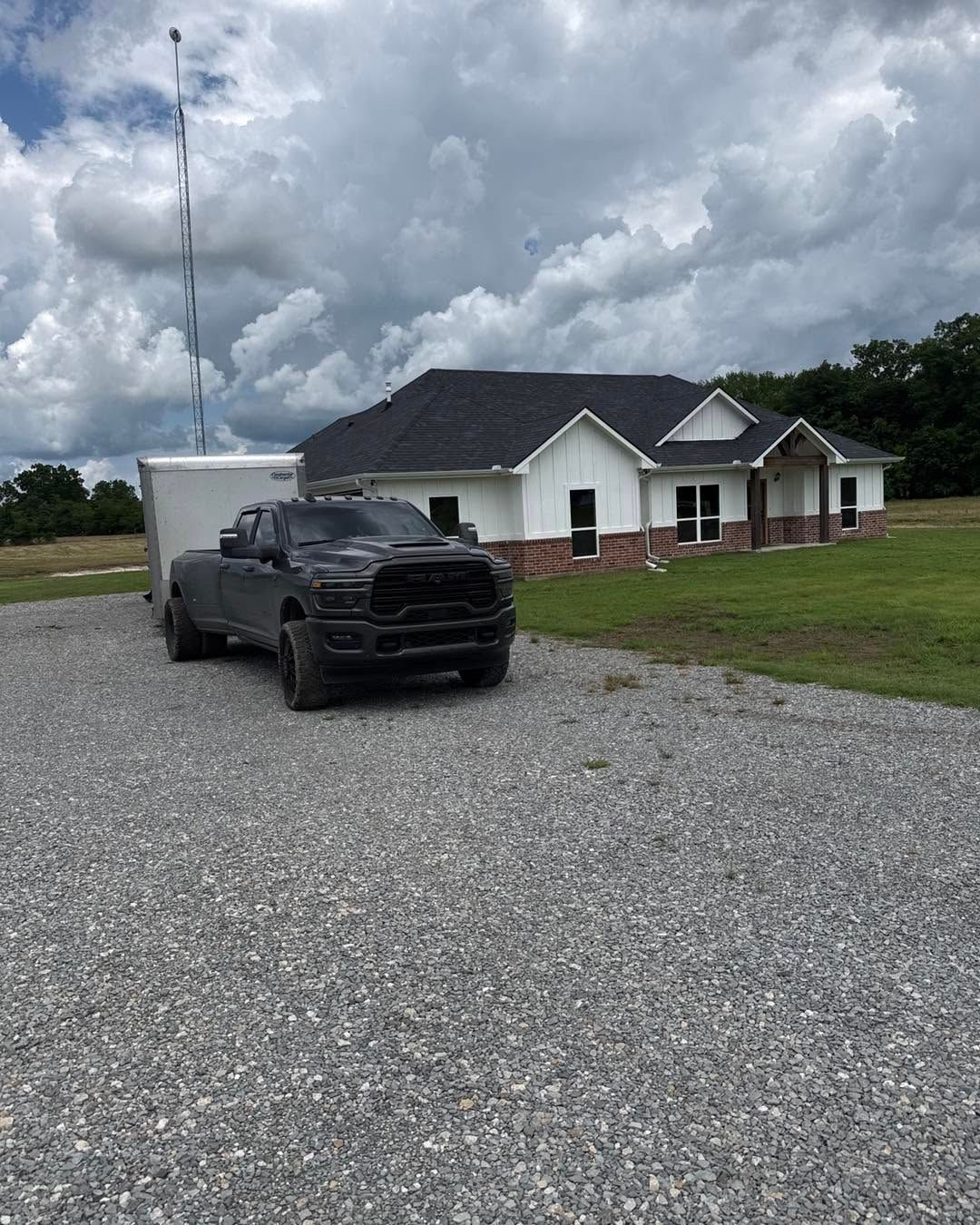 Black pickup truck parked on gravel in front of a small white house under cloudy skies
