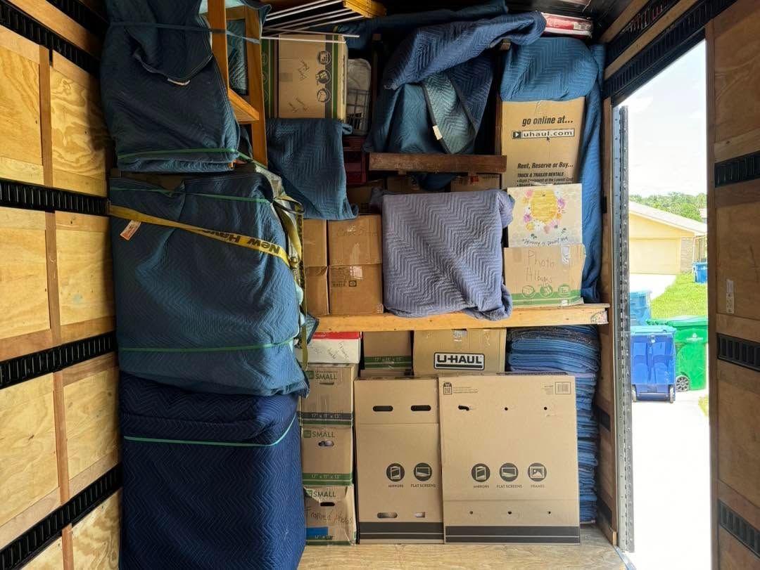 Packed moving truck loaded with boxes, wrapped furniture, and storage bins.