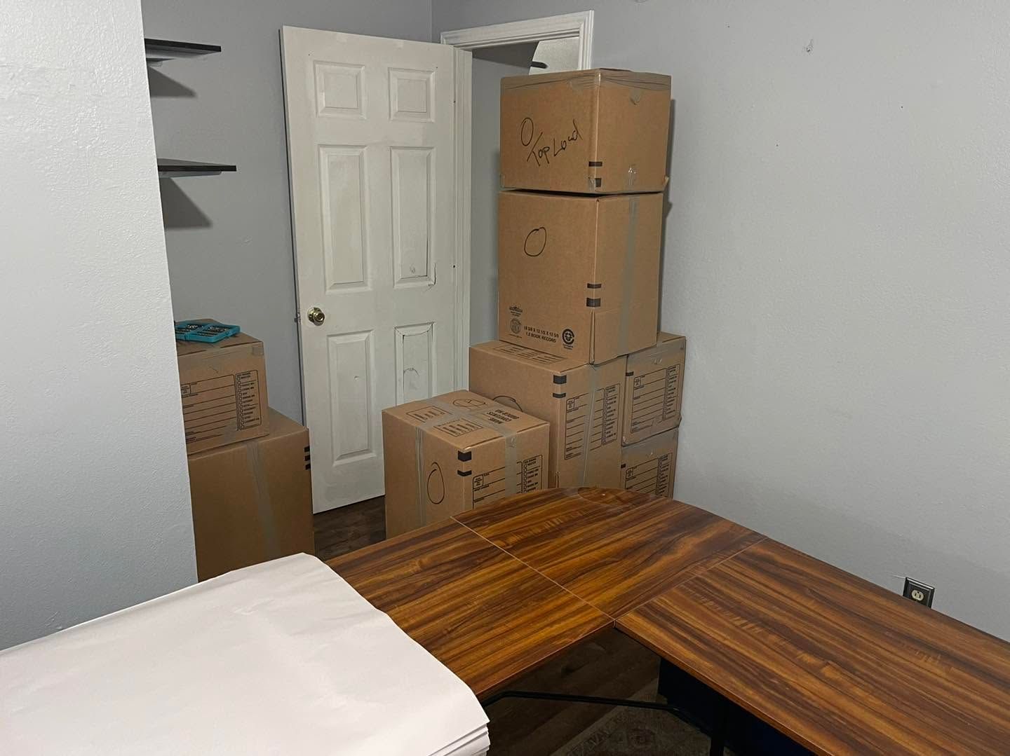 Unpacked moving boxes stacked by an open doorway in a room with a wooden desk and white furniture.
