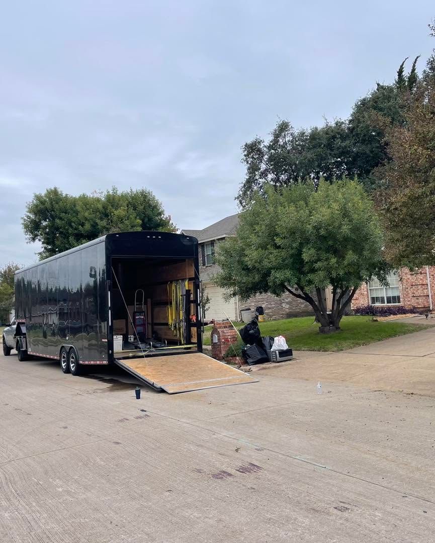 Black moving truck with open ramp parked outdoors; a few people are unloading items nearby.