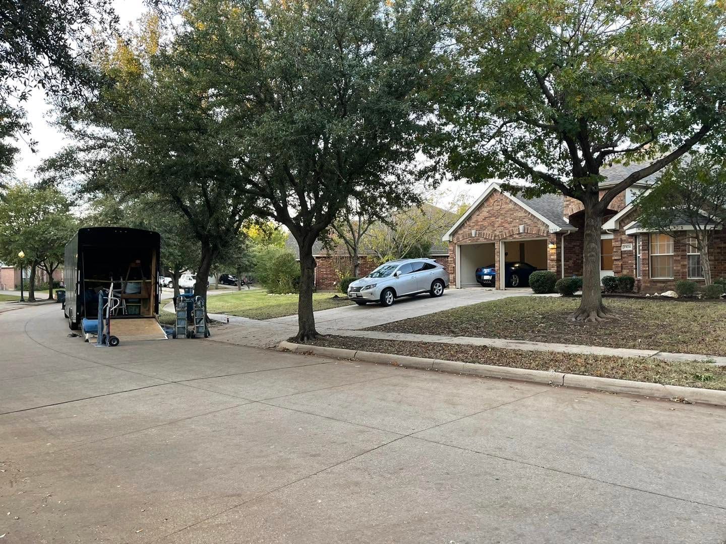Suburban street with trees, a parked car, and a moving truck beside a brick house