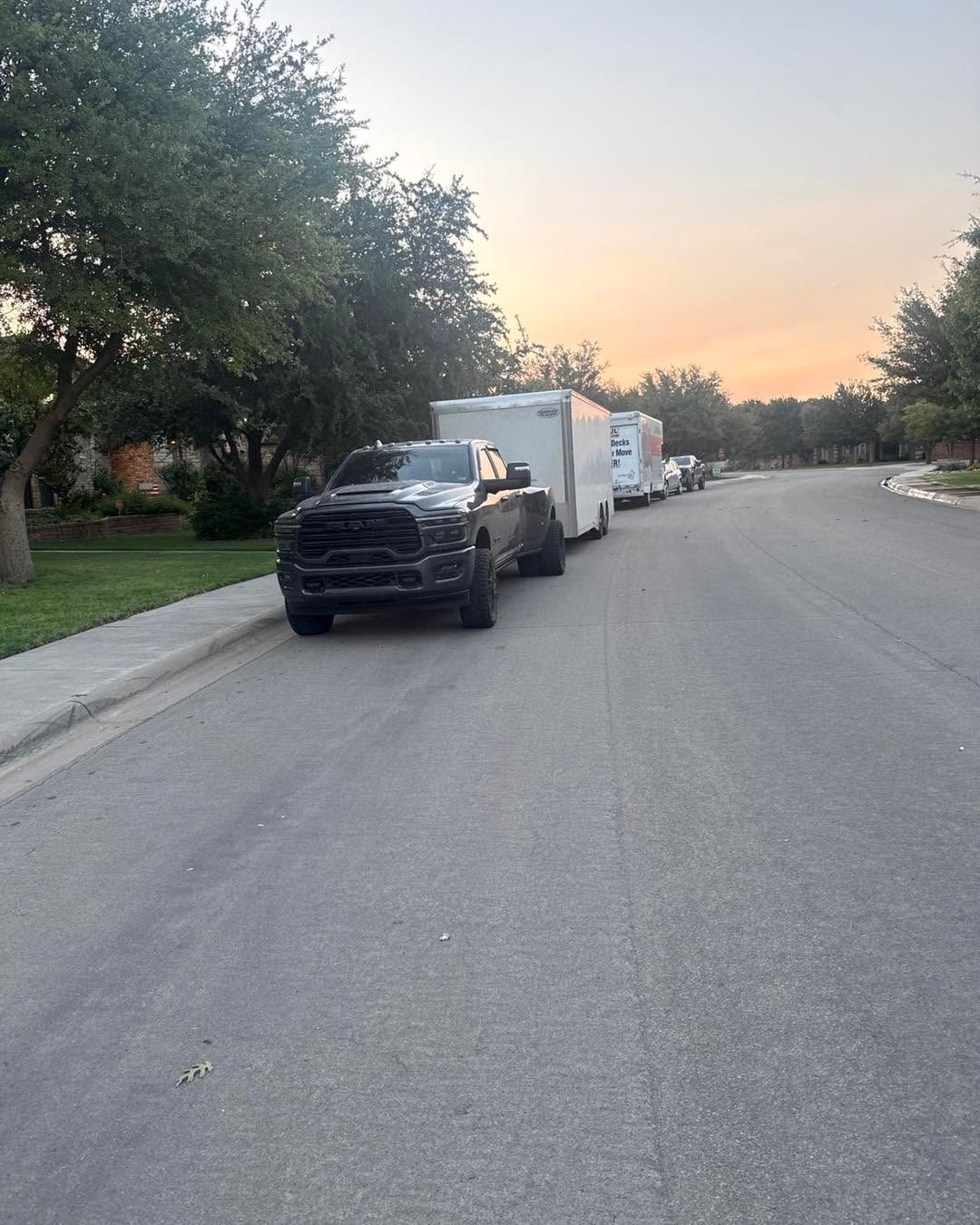 Parked black truck and white van lined along a quiet suburban street at sunset