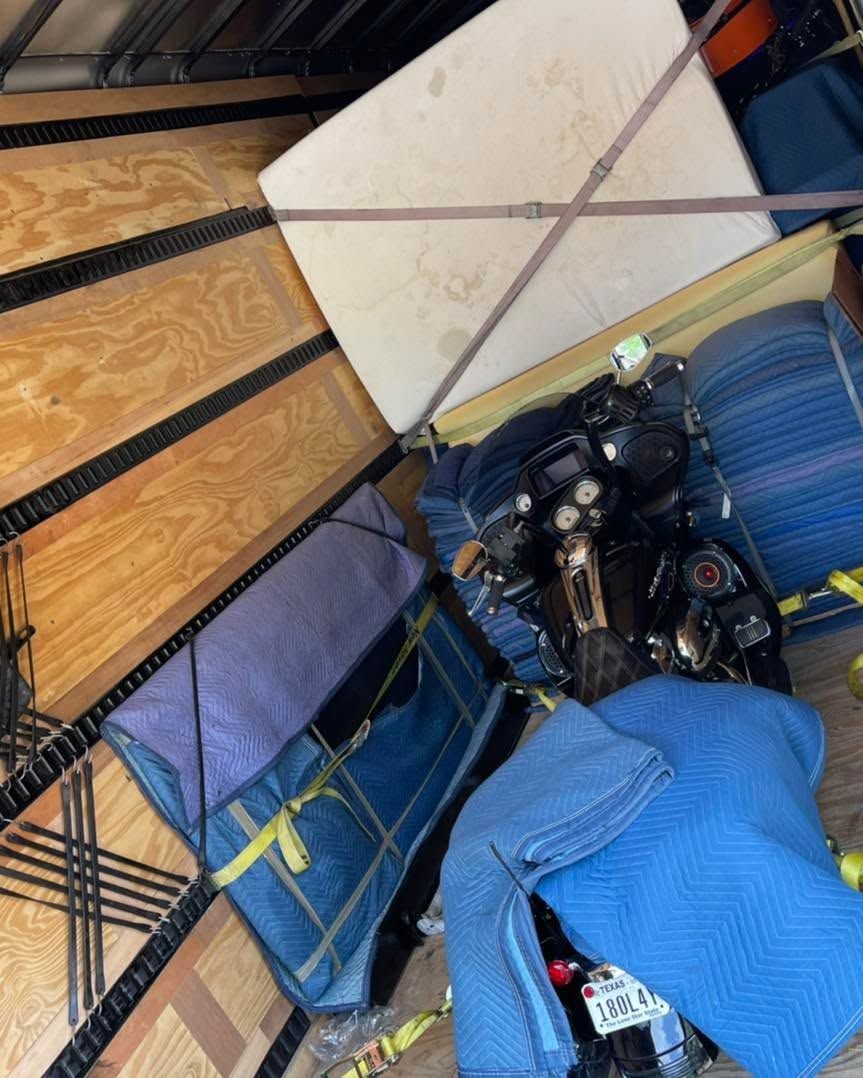 Cluttered storage area with folded blue mats, a black motorcycle, and stacked boards or boxes.