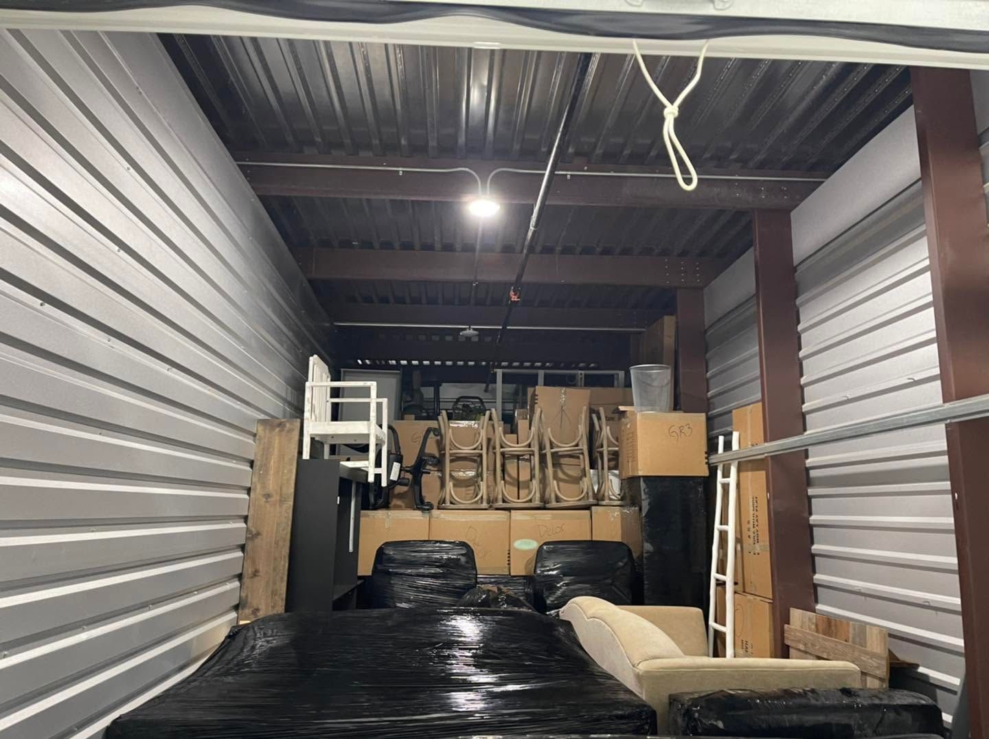Storage unit with stacked furniture and wrapped items, viewed from the doorway.