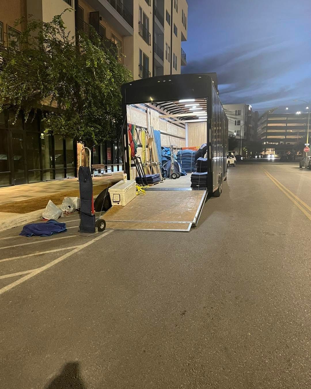 Portable trailer kiosk with open side lit at night on a quiet street beside apartment buildings.