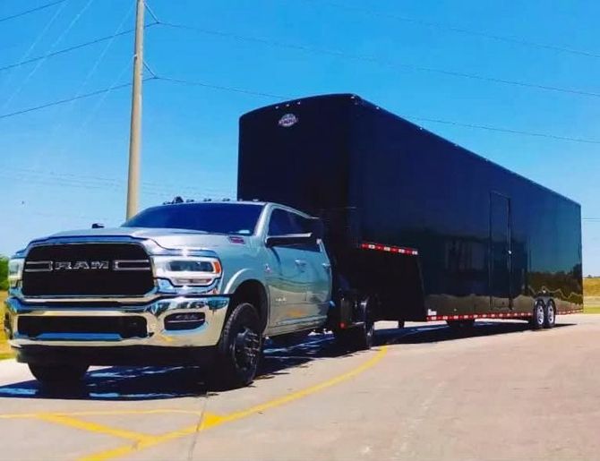 Silver pickup truck pulling a black enclosed trailer on a sunny road.