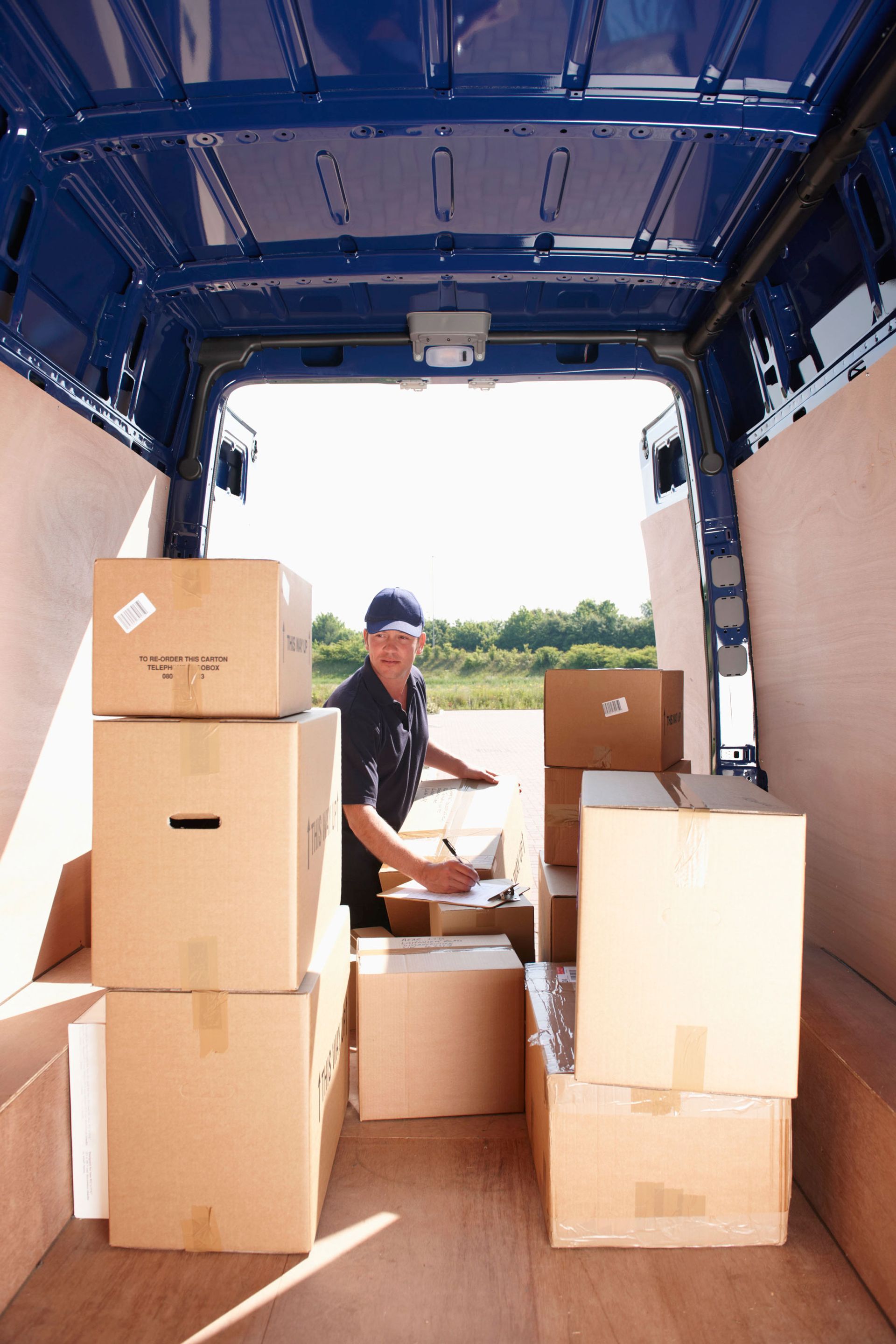 Person loading cardboard boxes into a truck with a blue cargo roof.