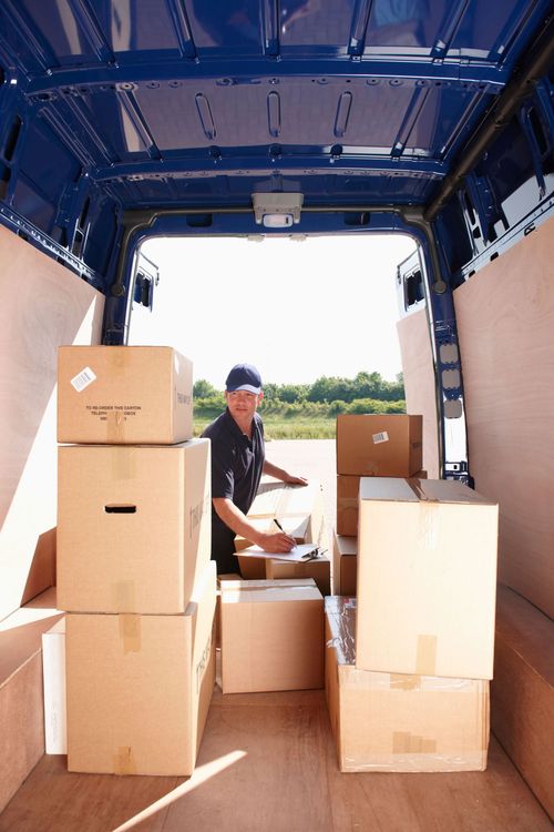 Worker loading stacked boxes into a delivery truck under a blue cargo canopy